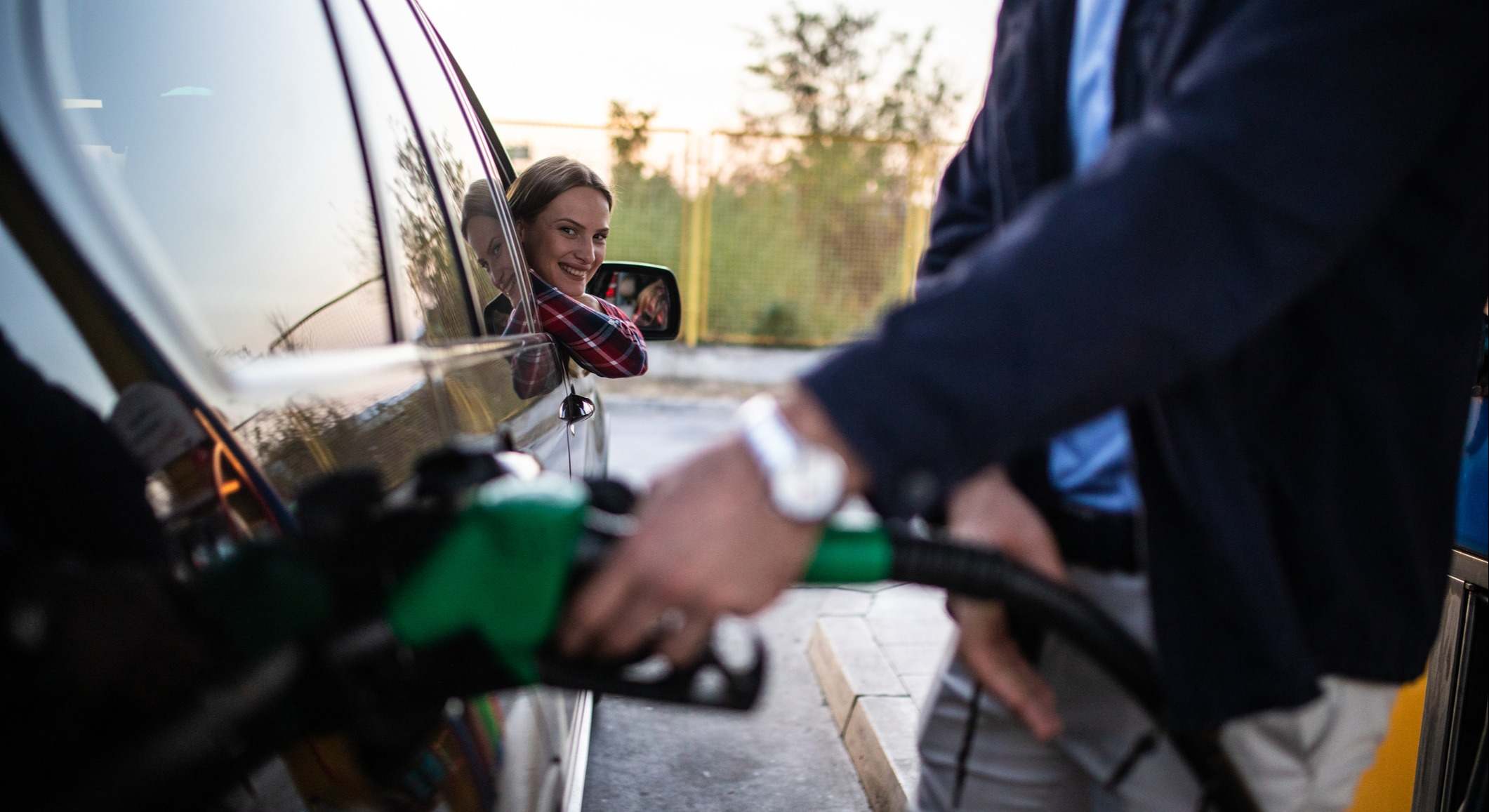 Mujer esperando al hombre mientras llena el tanque de un coche