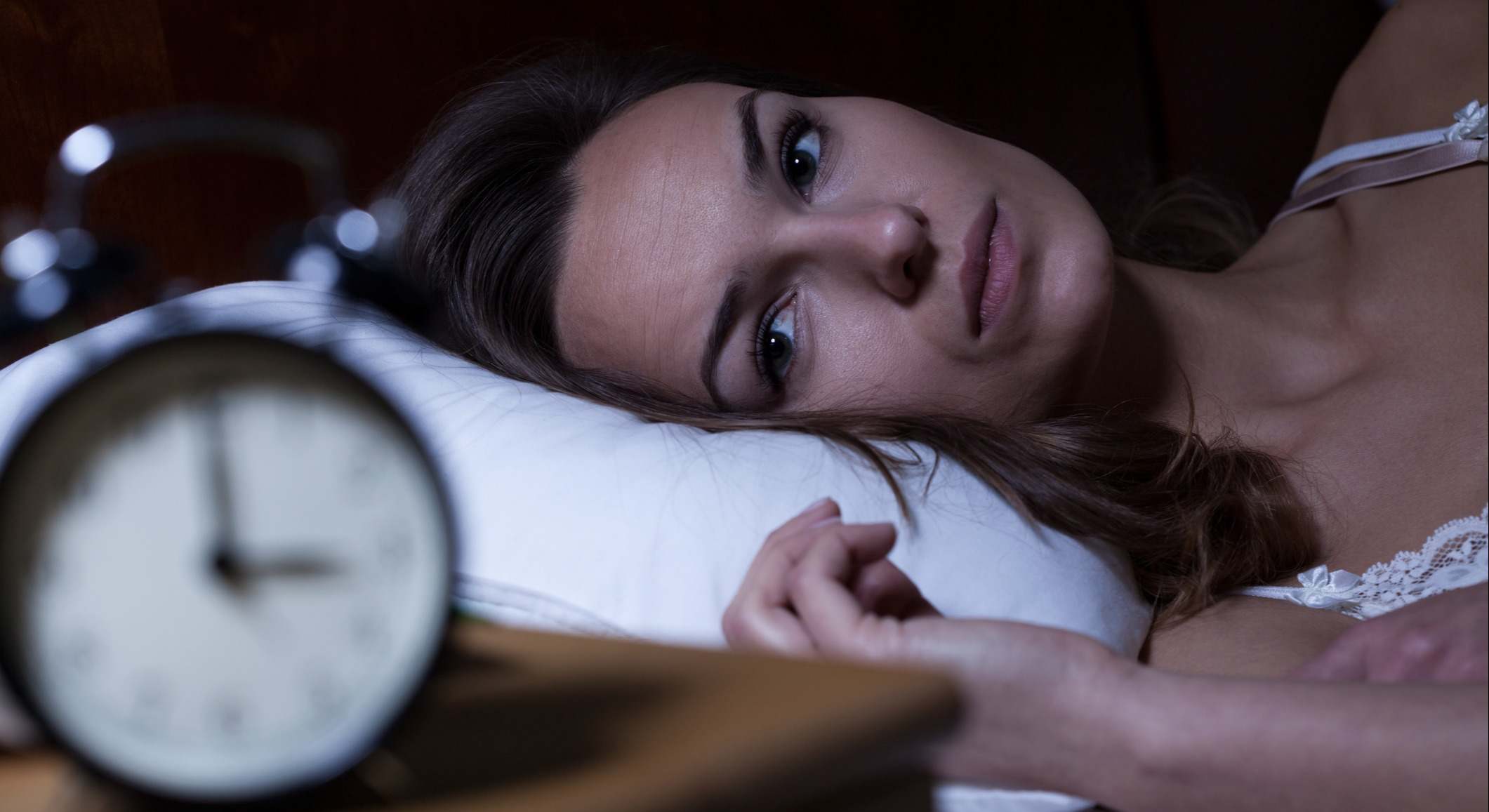 Mujer con insomnio en la cama mirando el reloj de la mesilla de noche