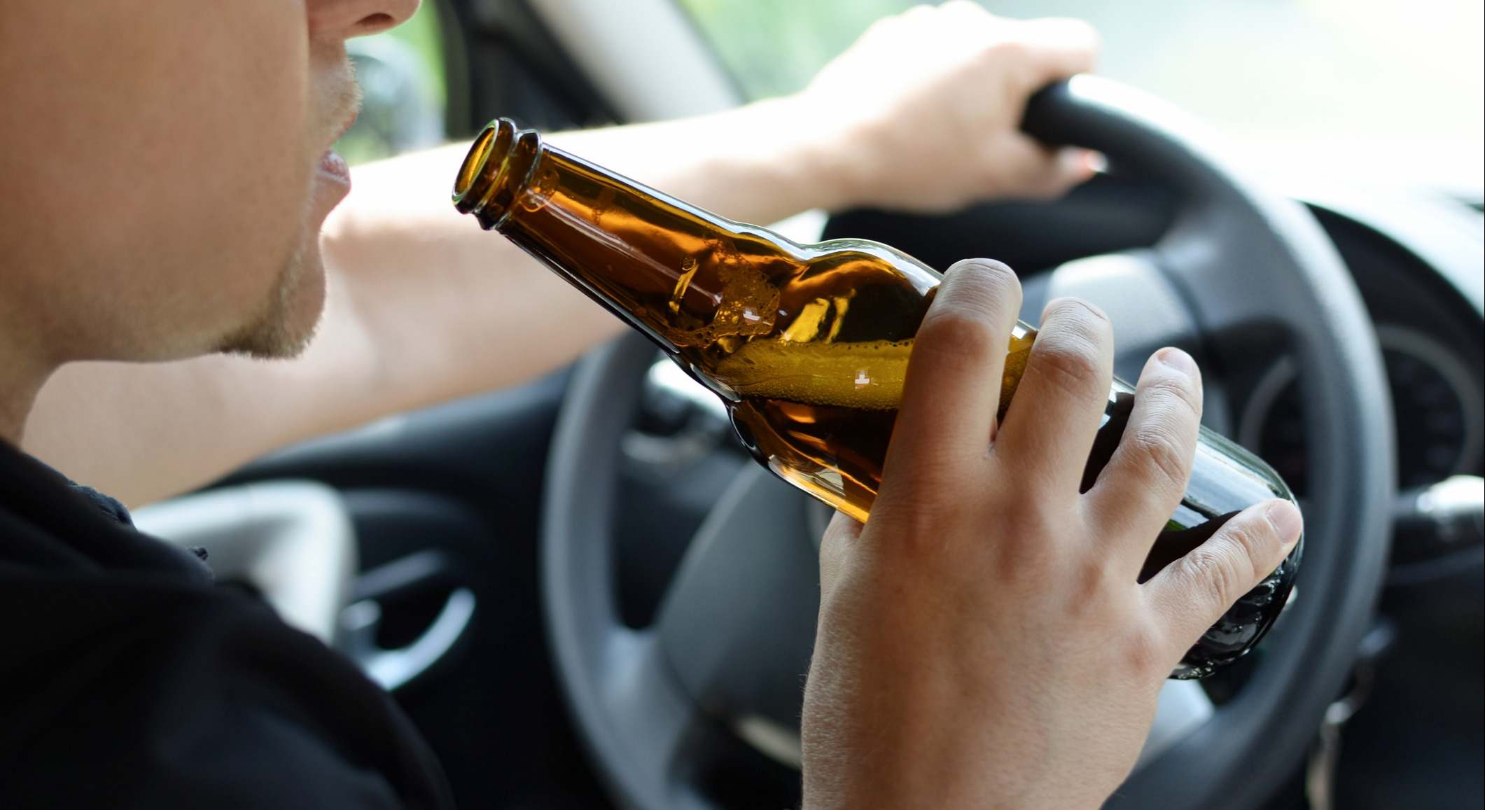 Hombre bebiéndose un botellín de cerveza al volante