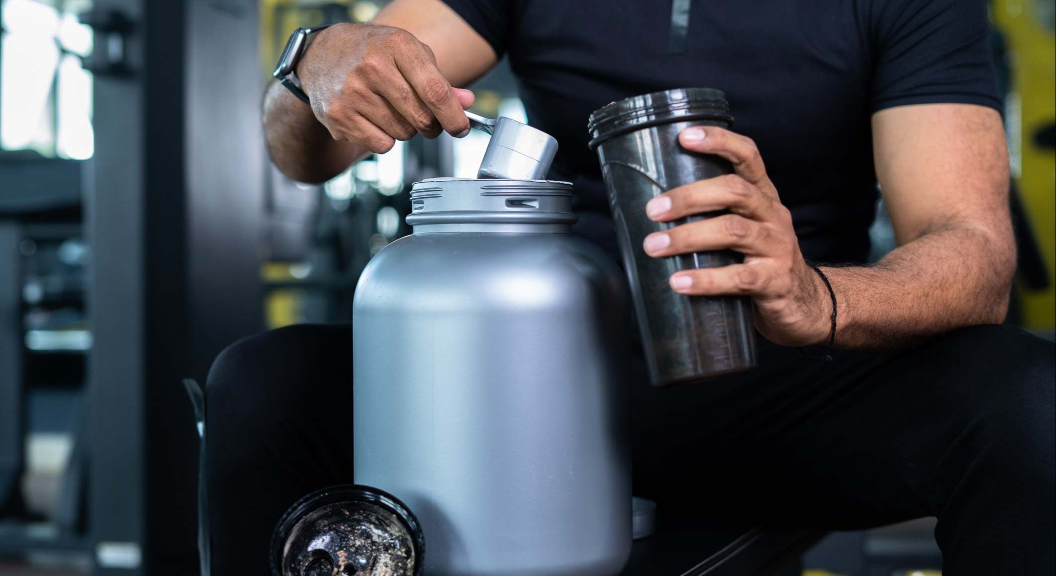 Primer plano de manos rellenando una botella con proteína en polvo en un gimnasio