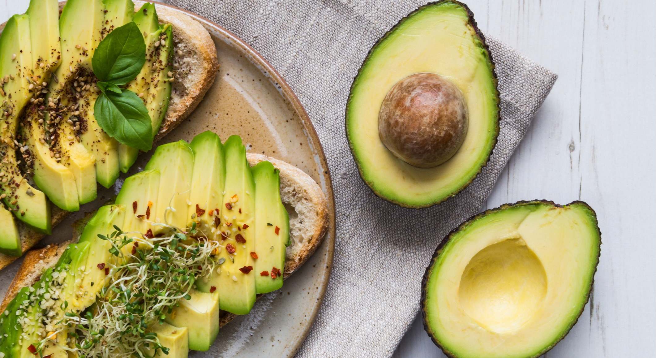 Tostadas con aguacate y berro y un aguacate partido a la mitad sobre una mesa