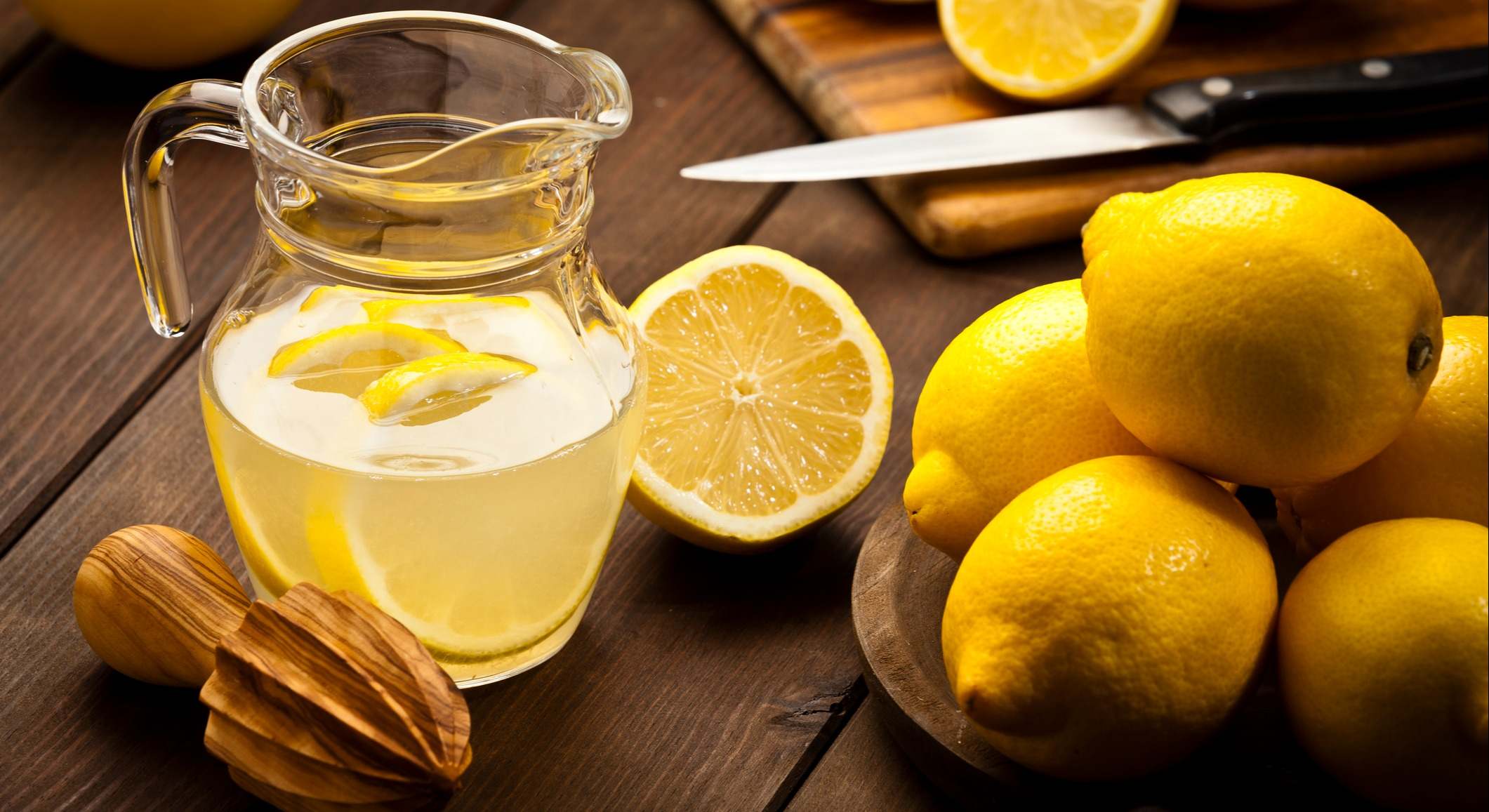 Limones y una jarra de limonada sobre una mesa de madera