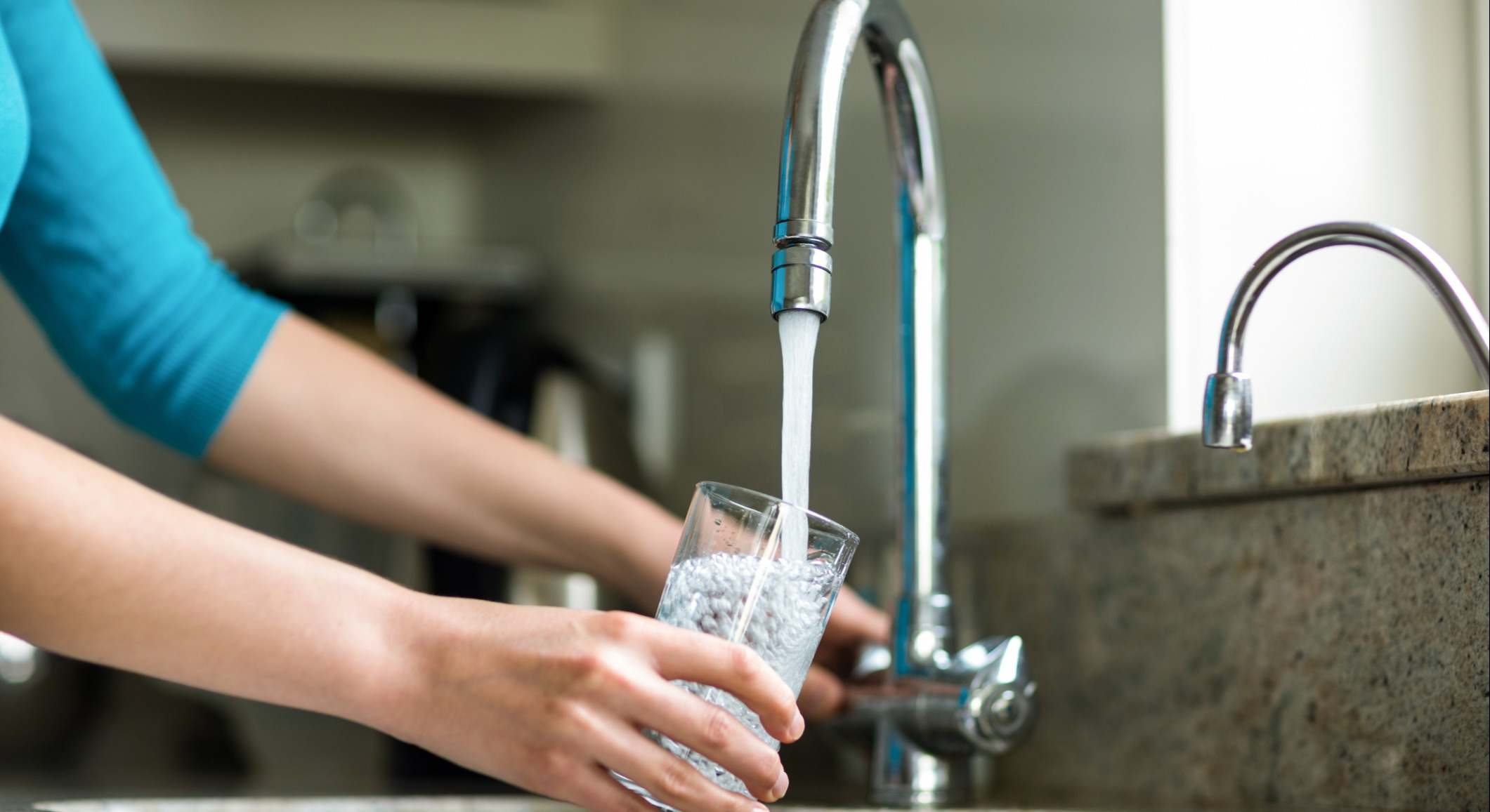 Una señora llena un vaso de agua en el grifo de su cocina