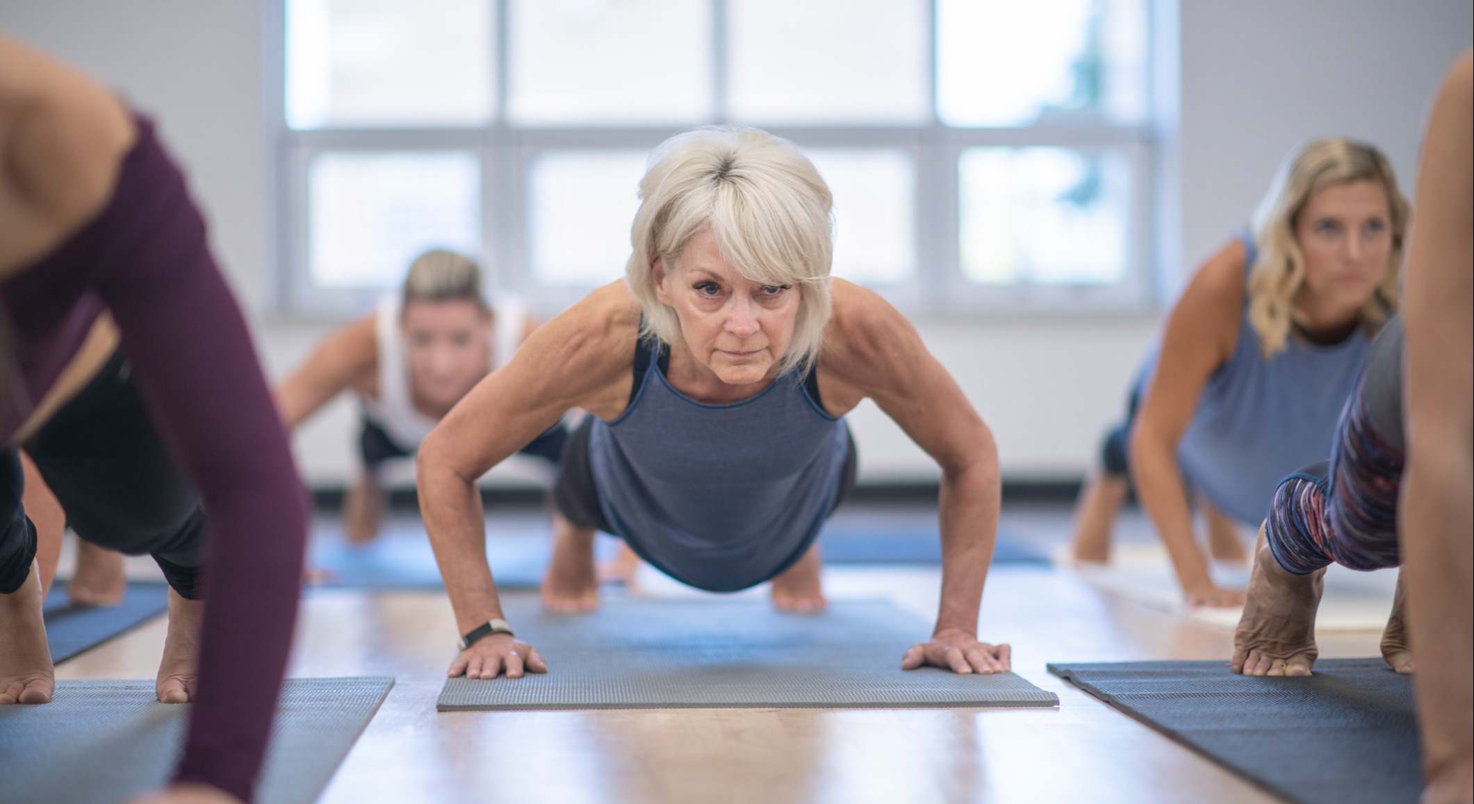 Mujer realizando ejercicios en un gimnasio en una esterilla junto a más mujeres