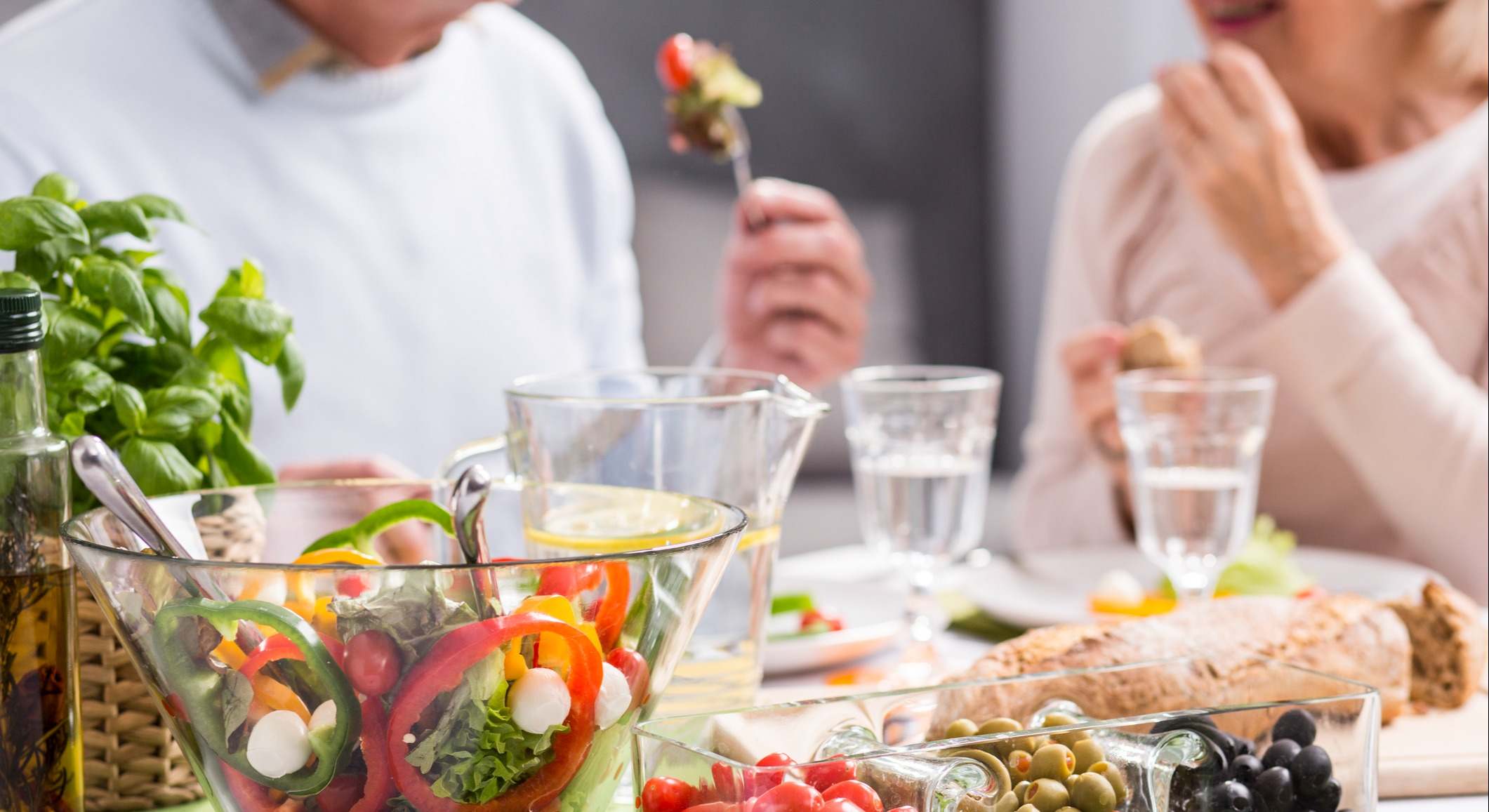 Pareja de personas mayores comiendo en una mesa con una ensalada