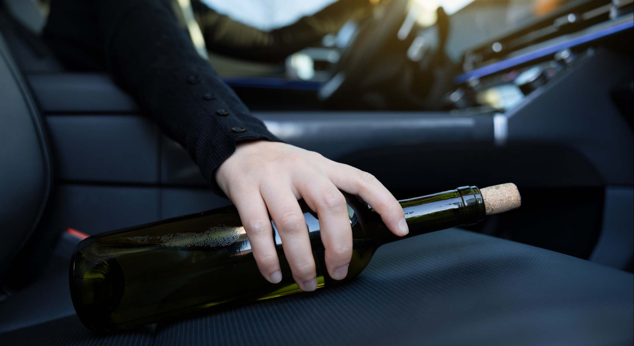 Persona cogiendo una botella de vino del asiento copiloto del coche