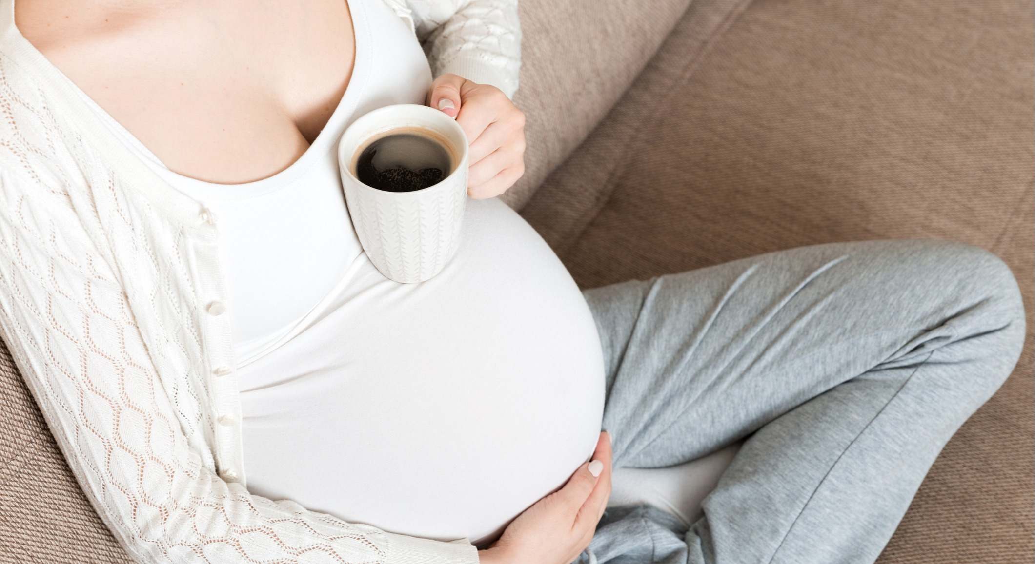 Chica embarazada sentada en el sofá con una taza de café en la mano