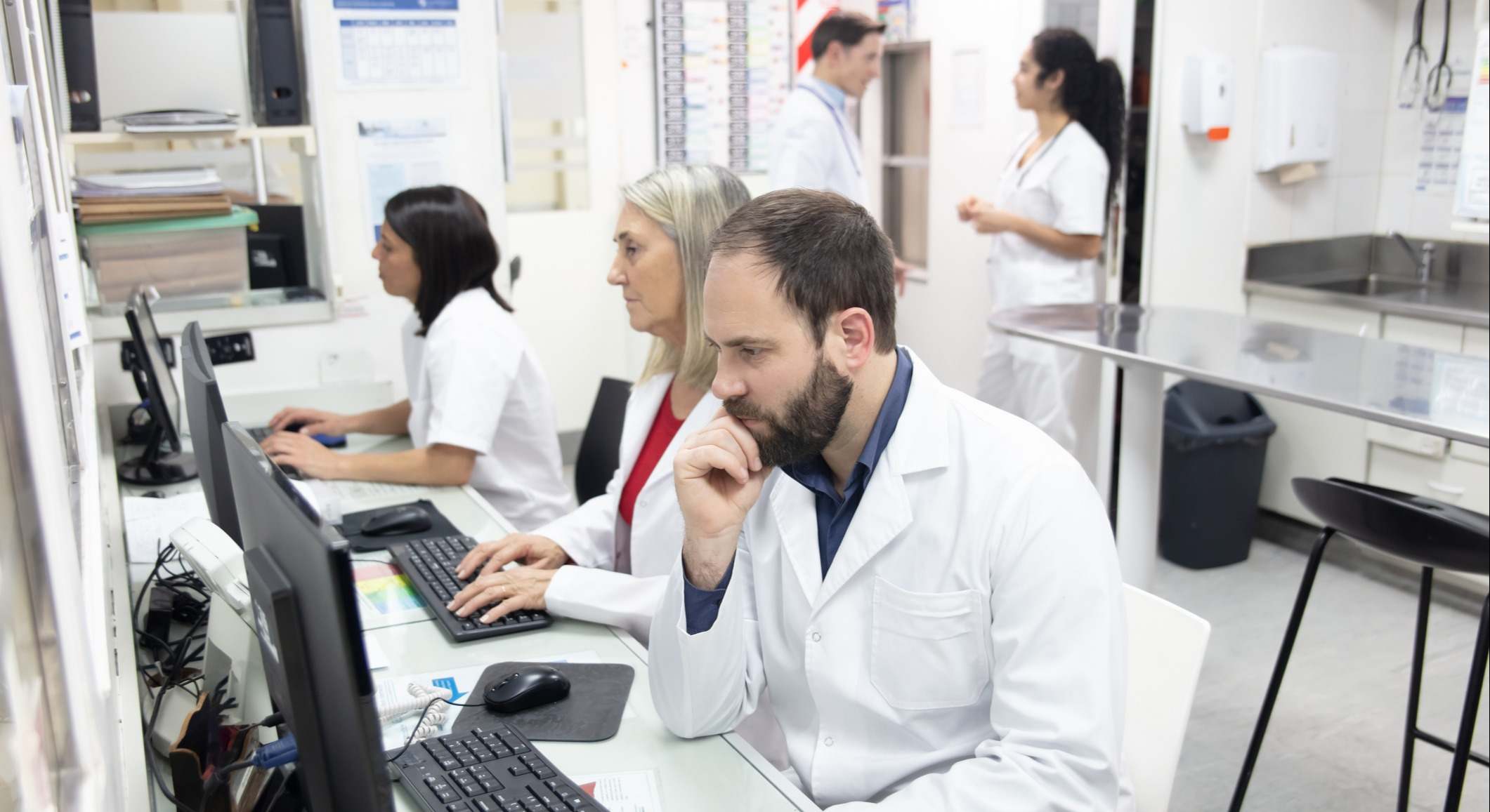 Equipo de trabajadores de la salud en la estación de enfermeras que trabajan en las historias clínicas de los pacientes utilizando computadoras