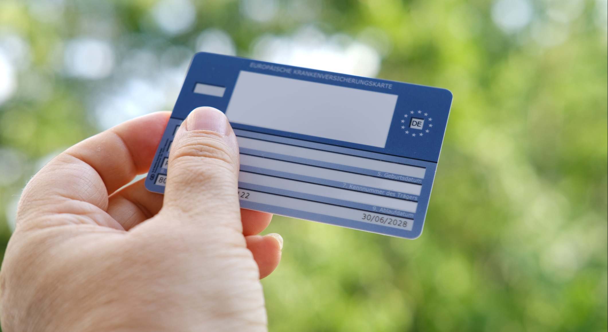 Tarjeta Sanitaria Europea en una mano sobre fondo verde natural