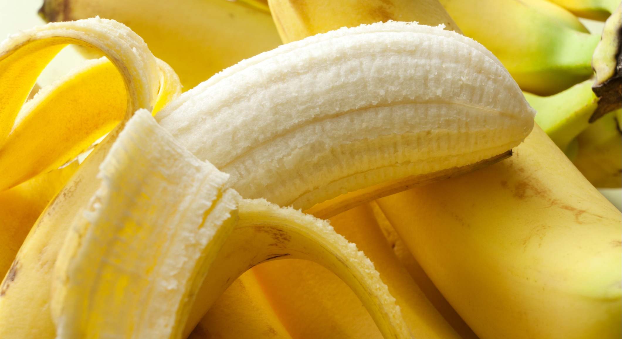 Plátano con la mitad de la piel quitada apoyado sobre más plátanos