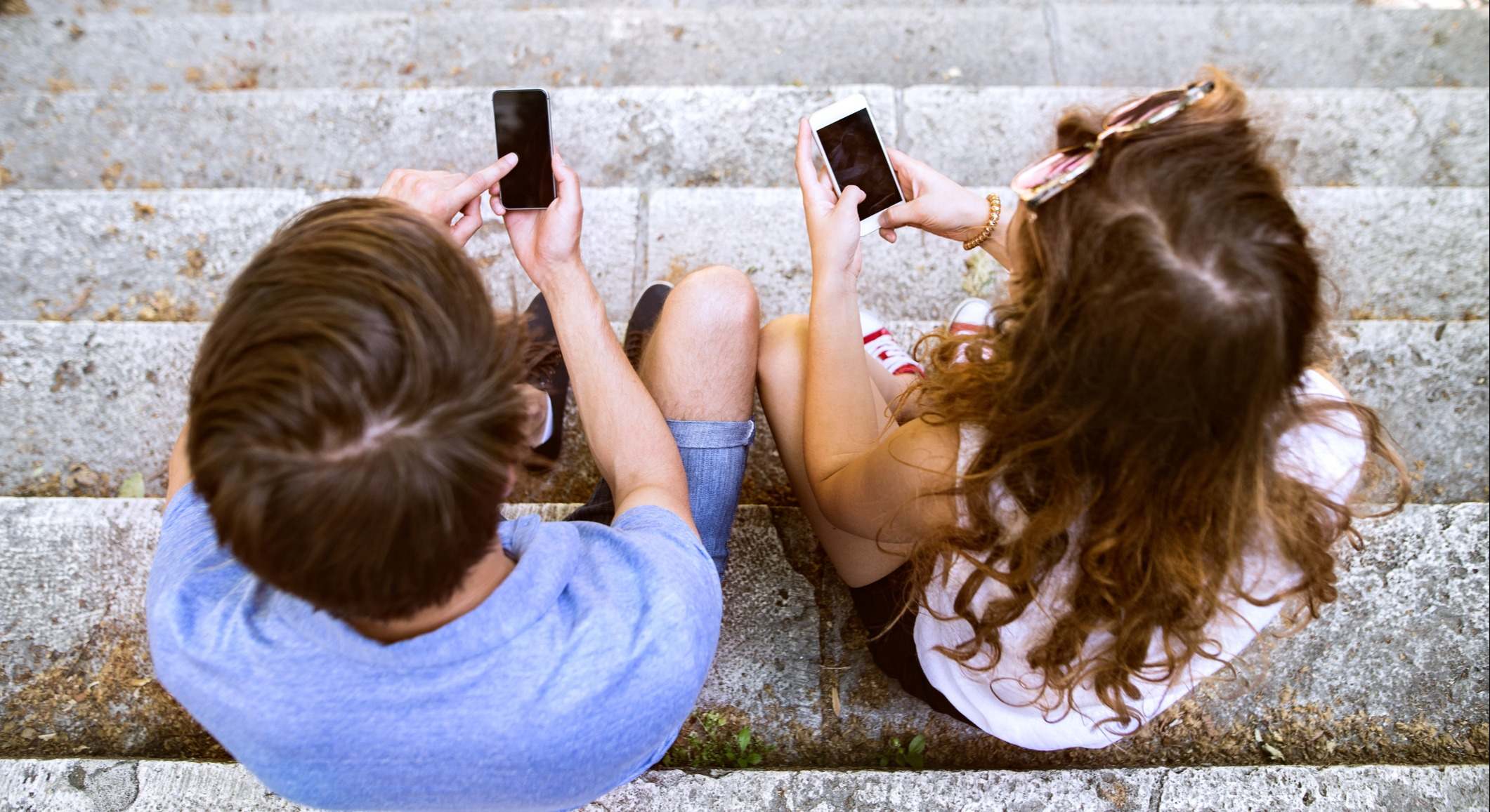 Una mujer y un hombre sentados en una escalera con los móviles en la mano. Foto: iStock