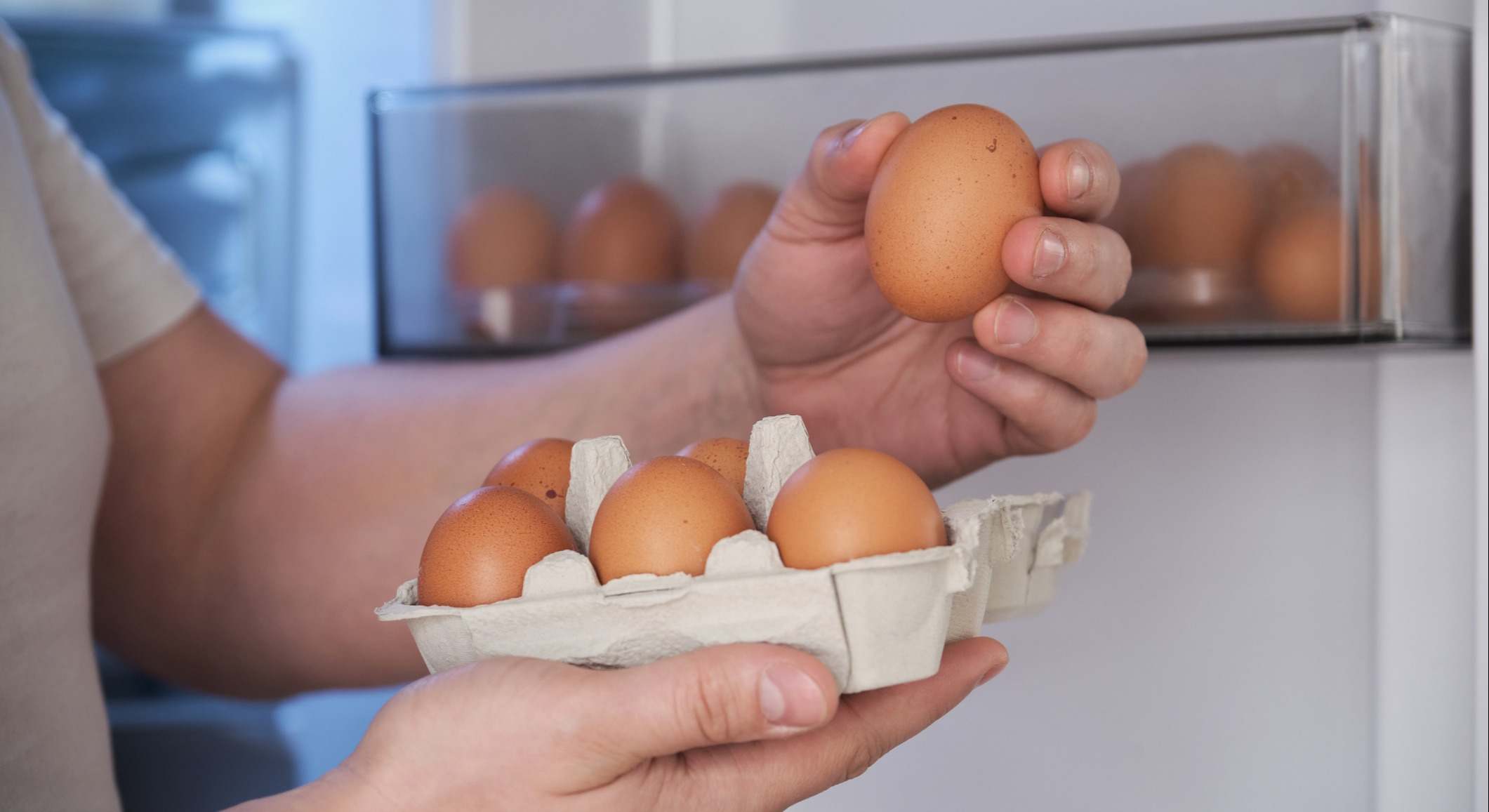 Primer plano de un hombre colocando huevos en el estante de la puerta de la nevera