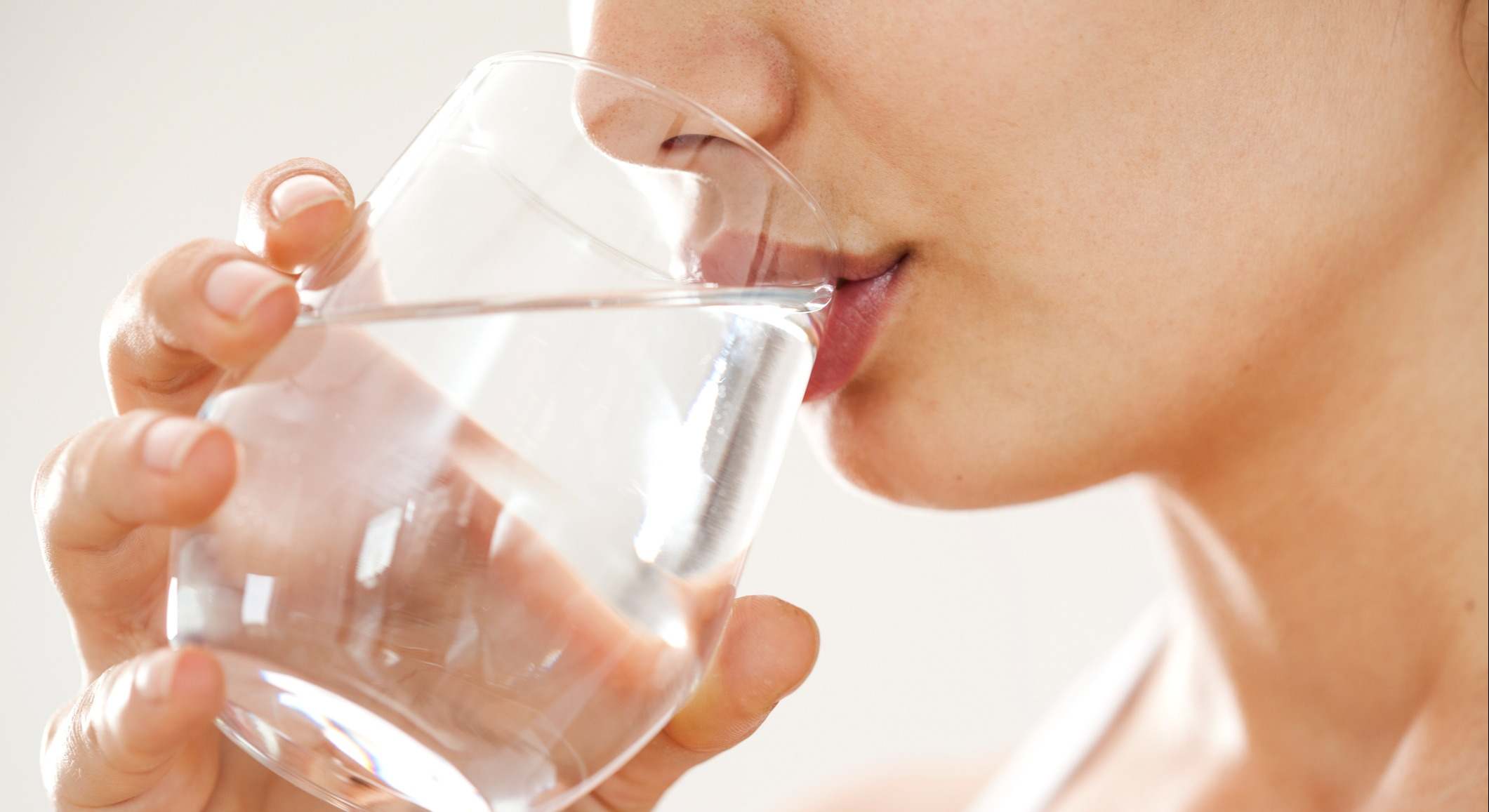 Una mujer bebe agua de un vaso de cristal. / Foto: iStock