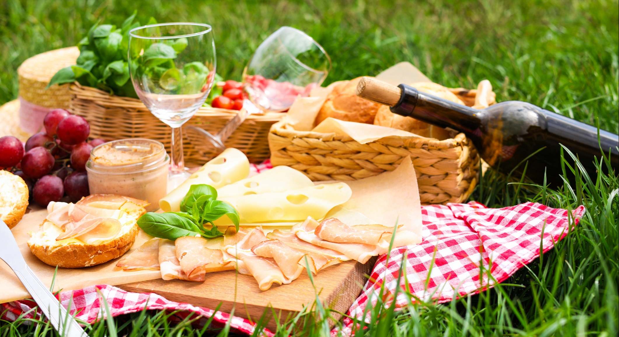 Manta de picnic con vino y comida sobre hierba verde