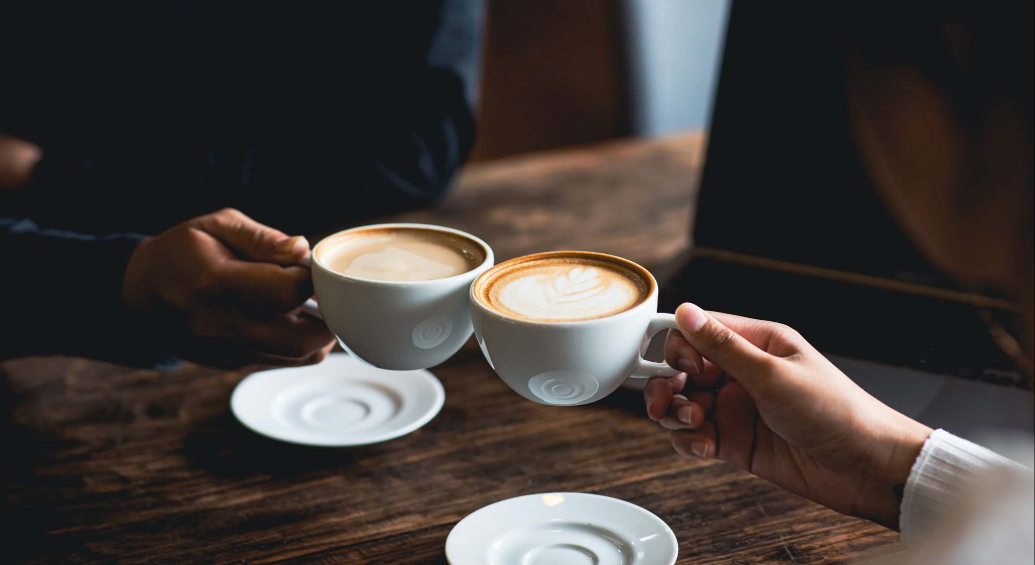 Personas brindando con su taza de café sentados en una mesa de madera