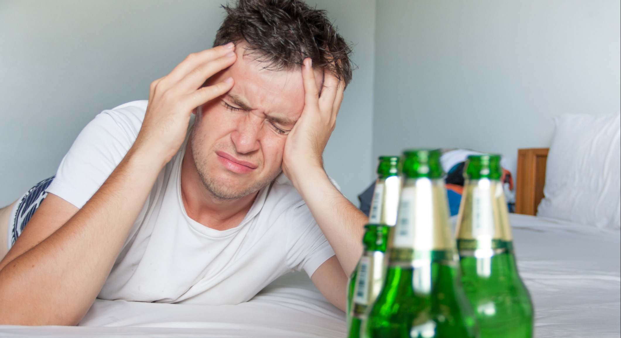 Hombre sufre resaca en la cama con botellas de cerveza
