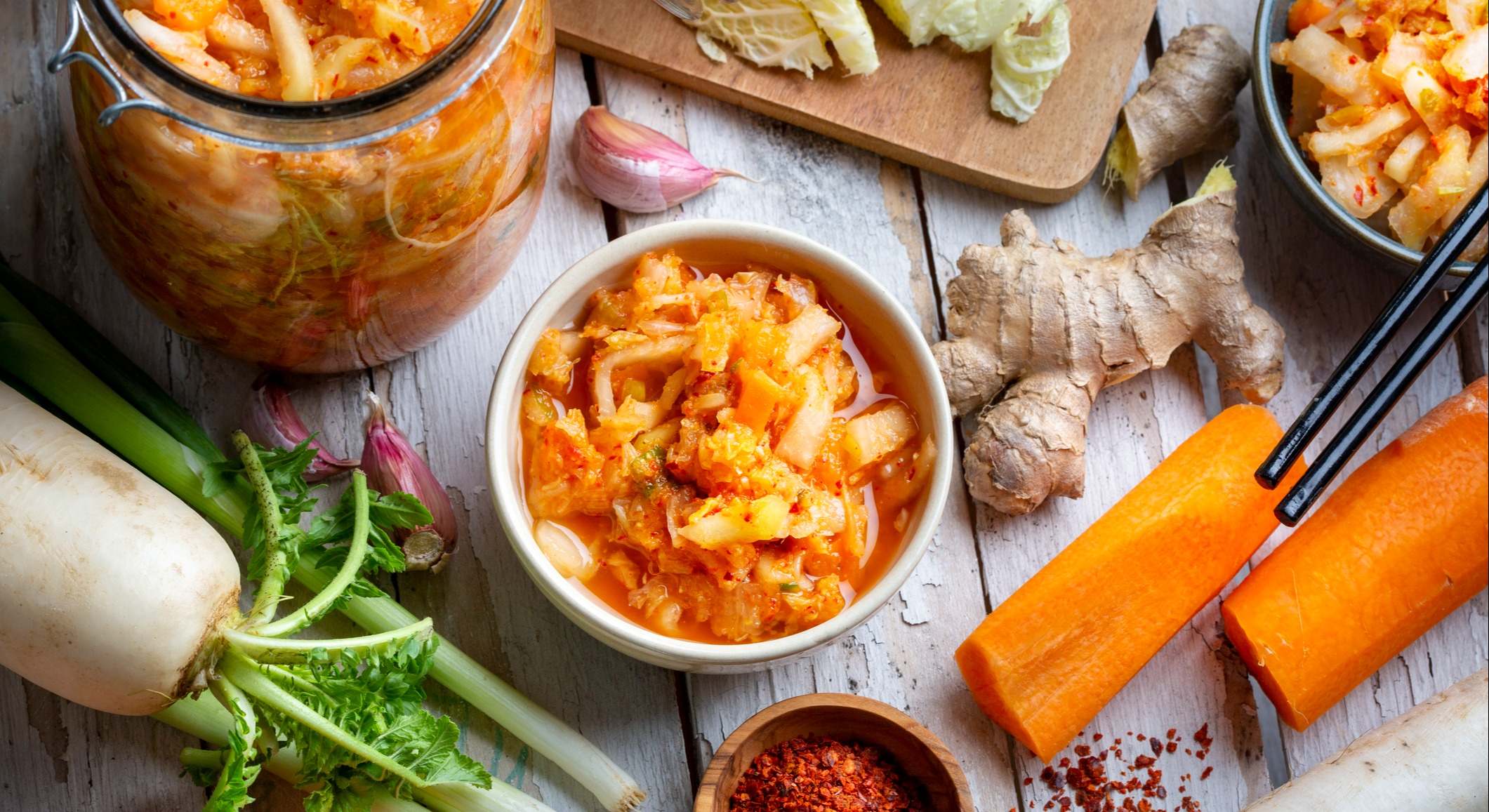 Plato de kimchi rodeado de verduras sobre una mesa de madera