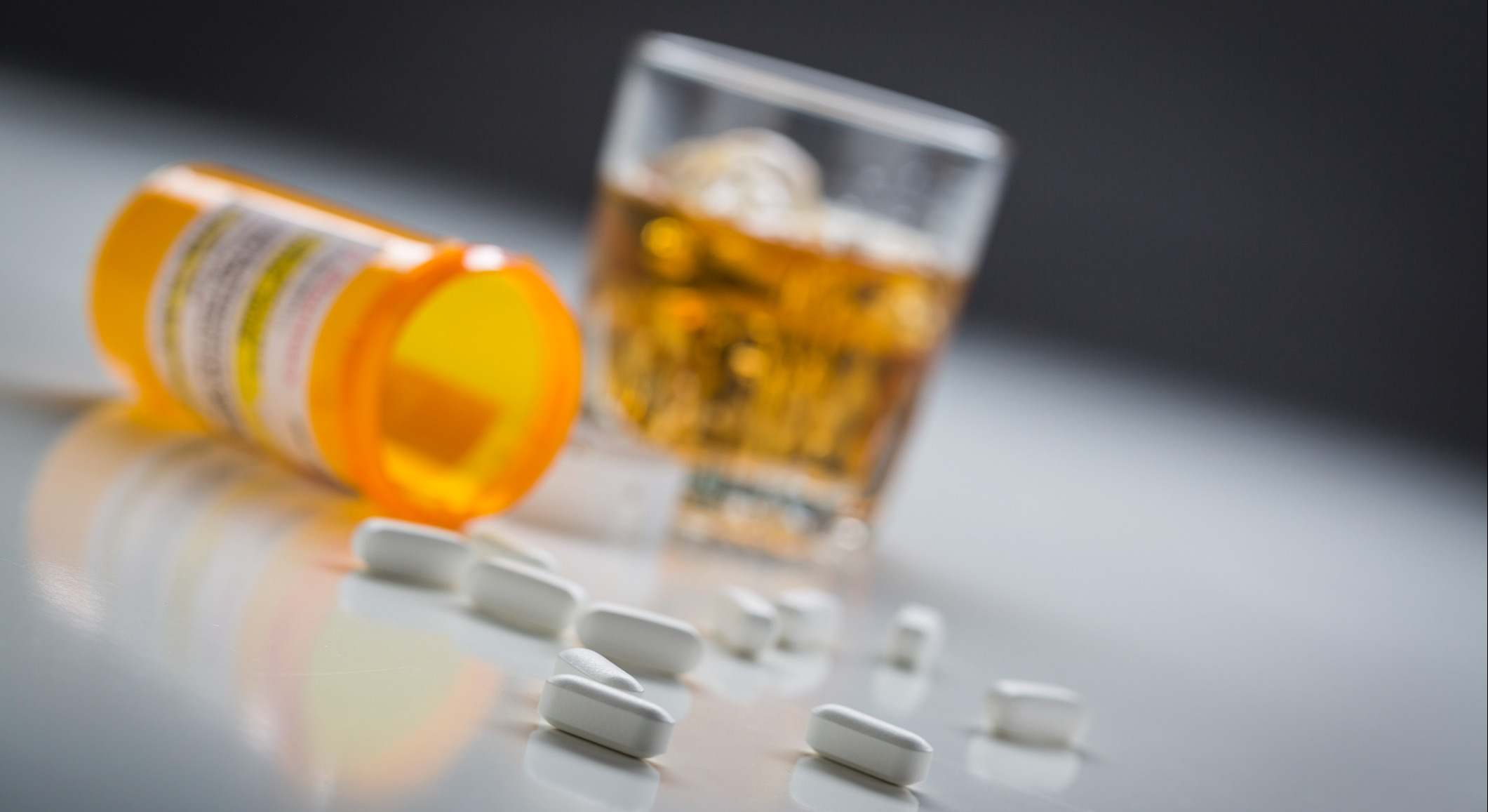 Píldoras derramadas cerca de un vaso de alcohol