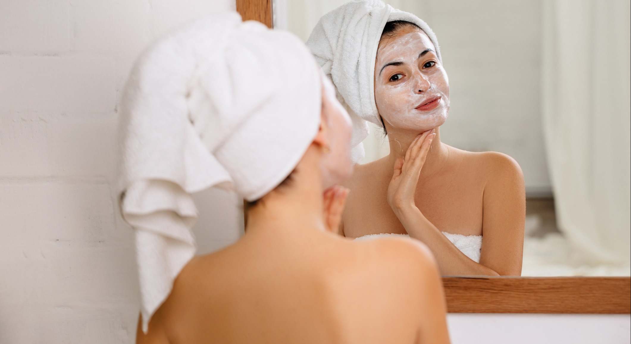 Mujer aplicándose una crema exfoliante en frente del espejo