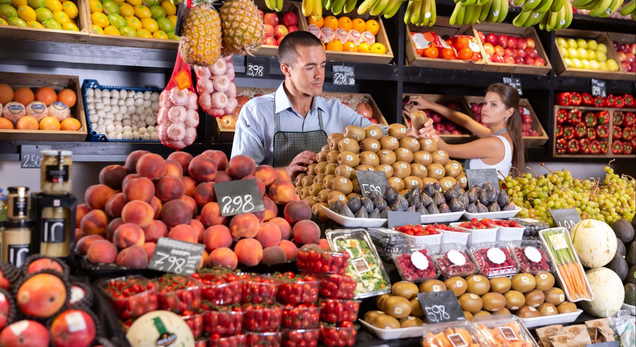 Vendedor sostiene kiwi cerca del mostrador de frutas