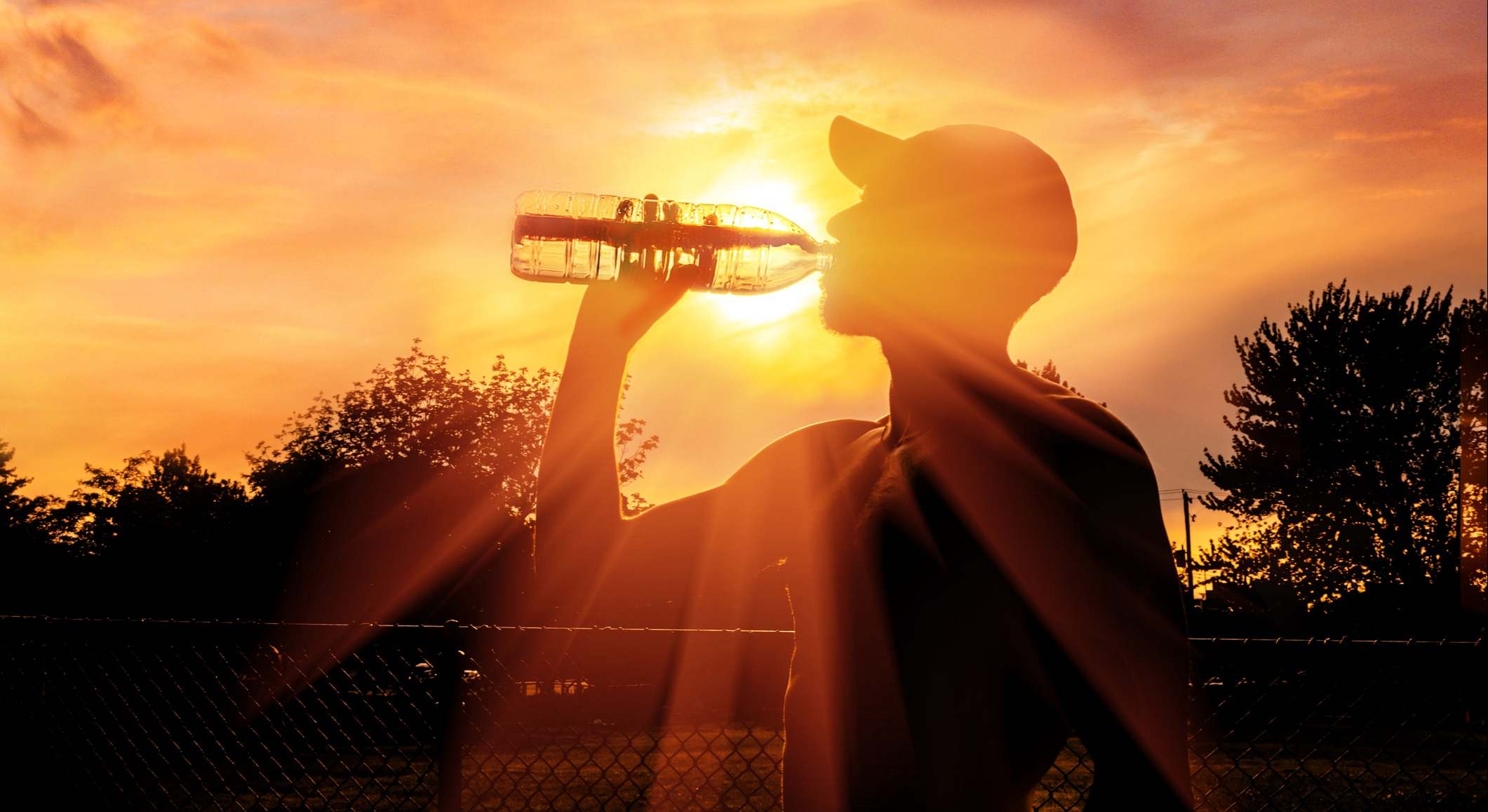 Un hombre bebiendo agua con el sol intenso de fondo