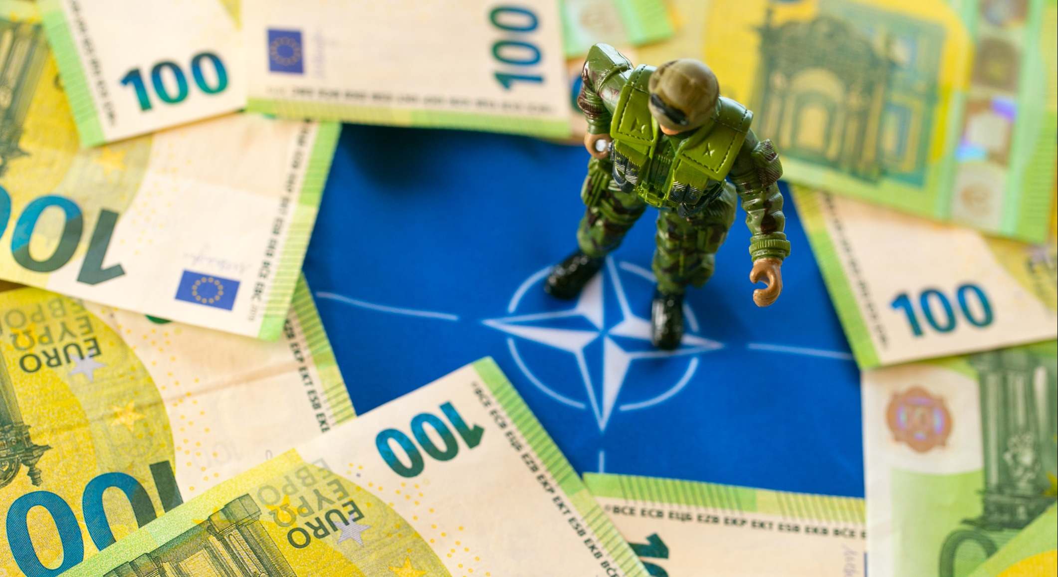 Un soldadito sobre una mesa con el logo de la OTAN y un montón de billetes de 100 euros