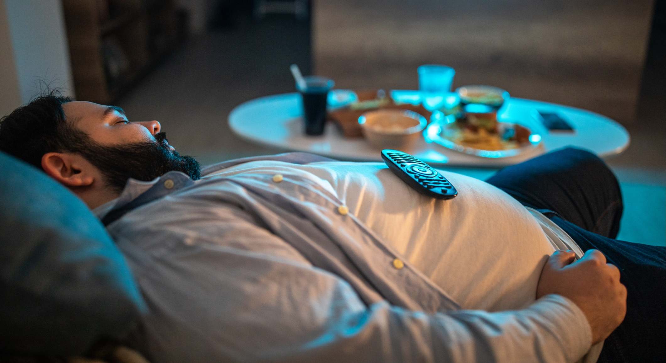 Hombre durmiendo después de cenar en el sofá de su casa