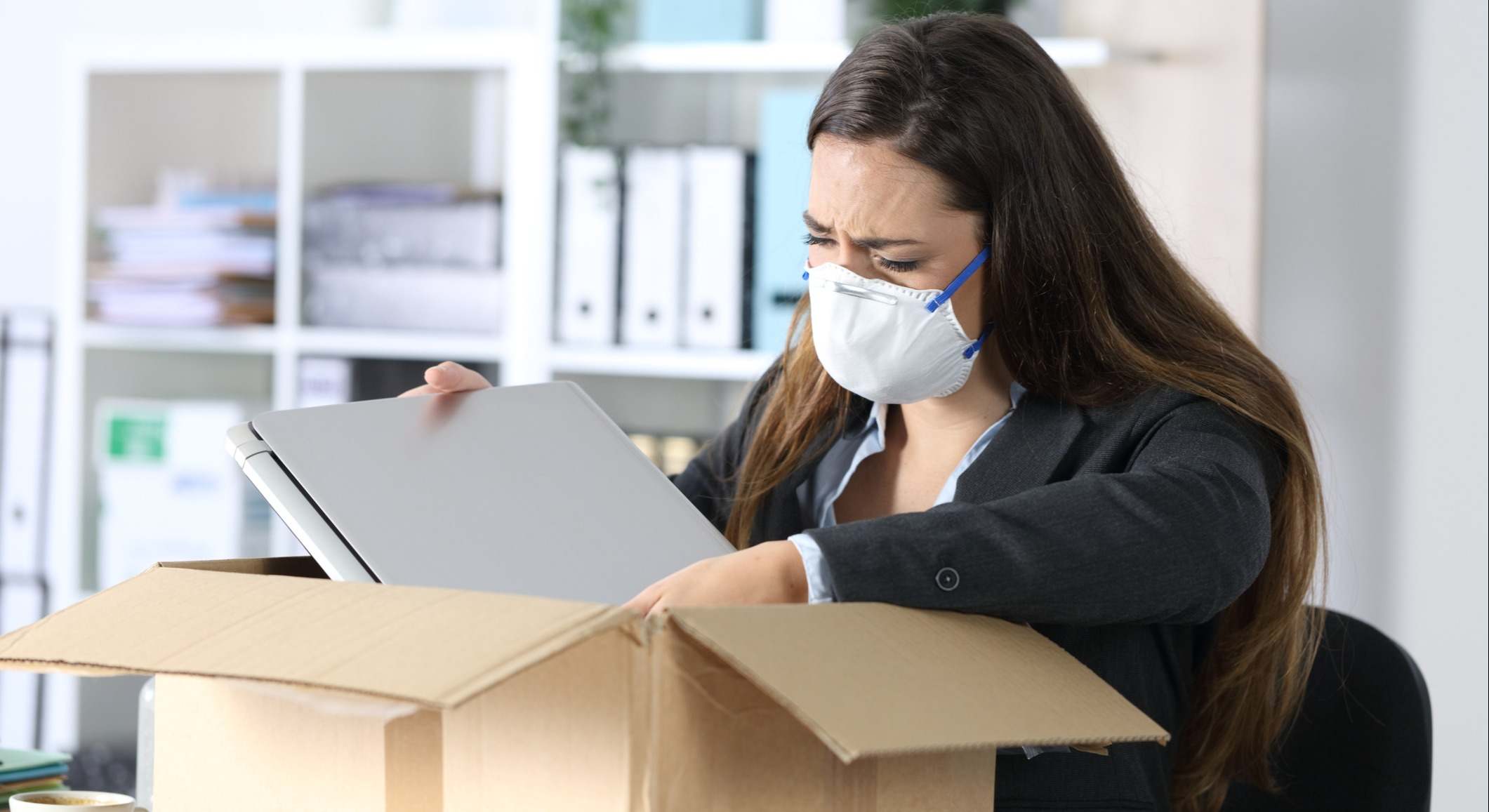 Trabajadora recogiendo sus pertenencias de la oficina con una mascarilla en la cara