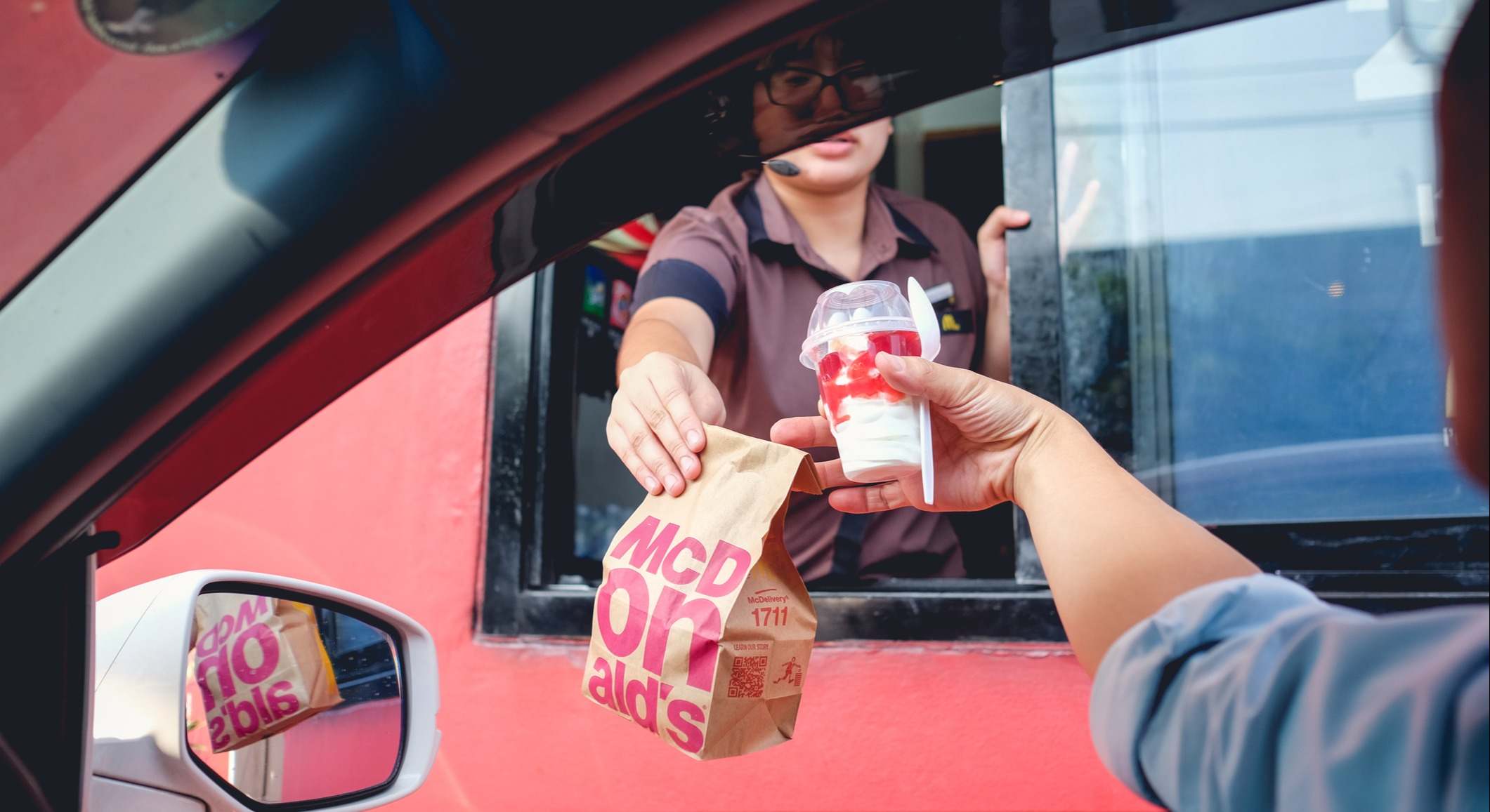 Trabajadora de Mcdonalds repartiendo un pedido a un cliente en su coche