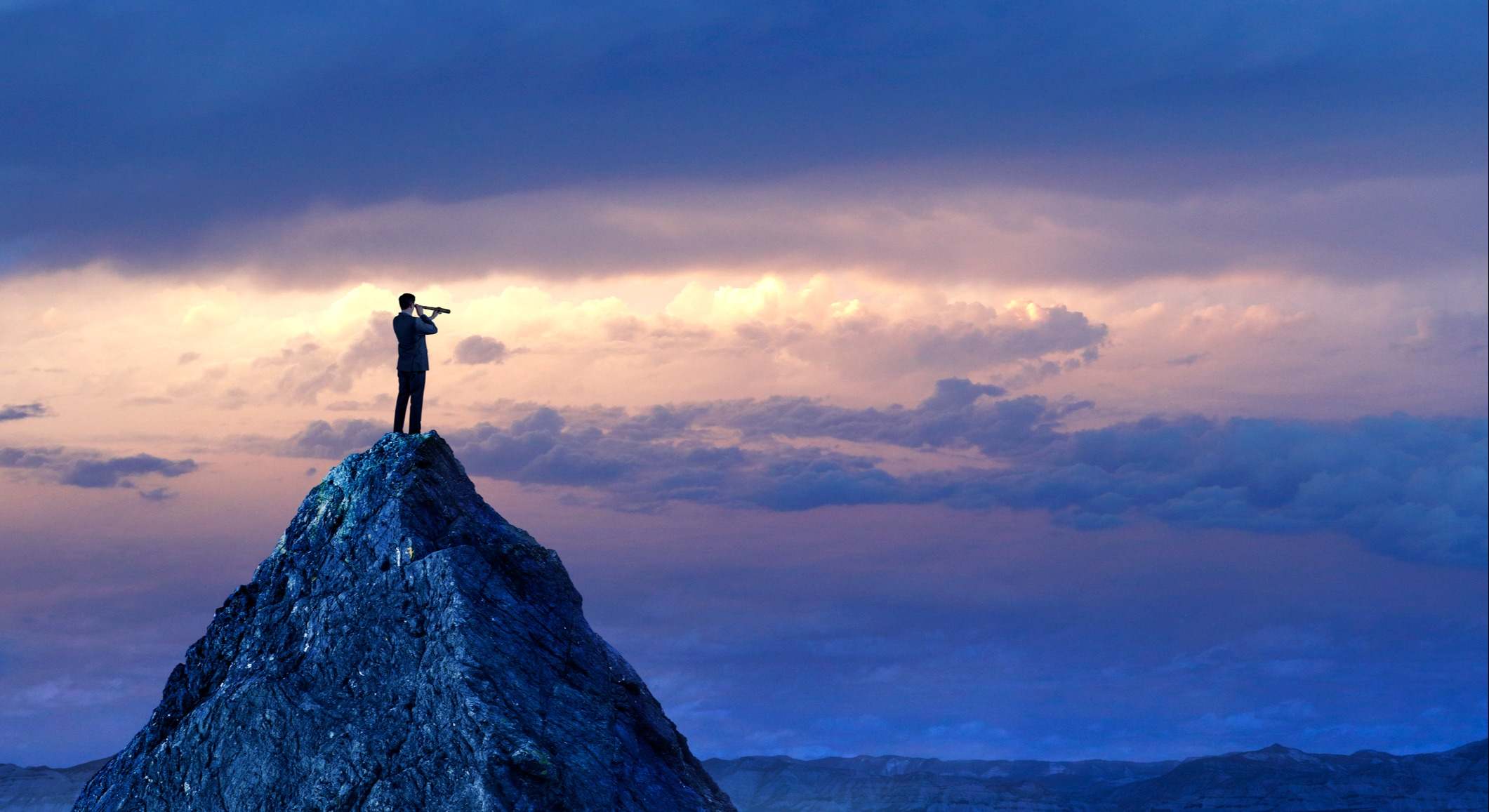 Una persona subida sobre el pico de una montaña observa el horizonte con un catalejo