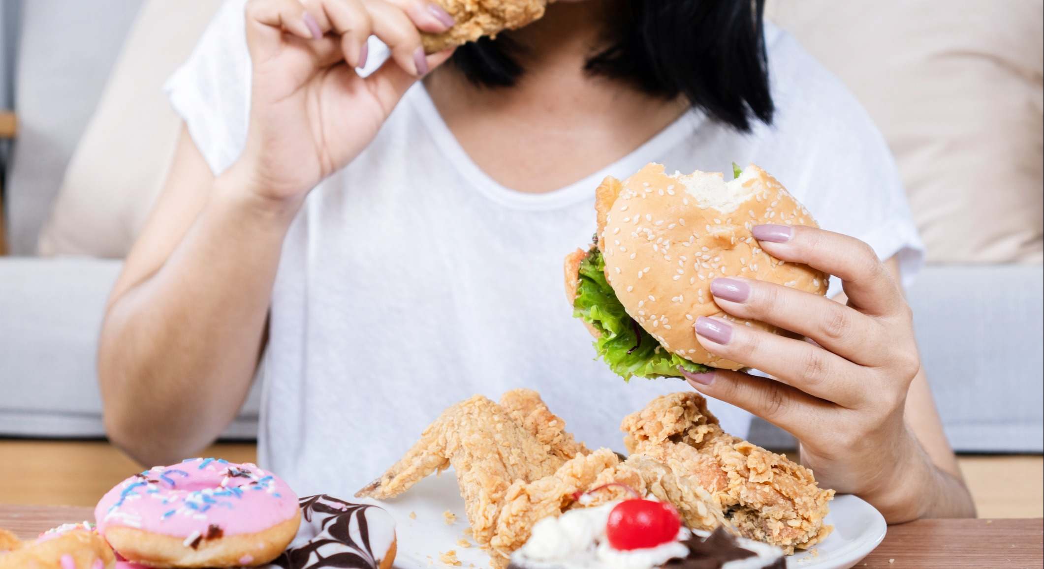 Mujer comiendo hamburguesa, pollo frito y postres