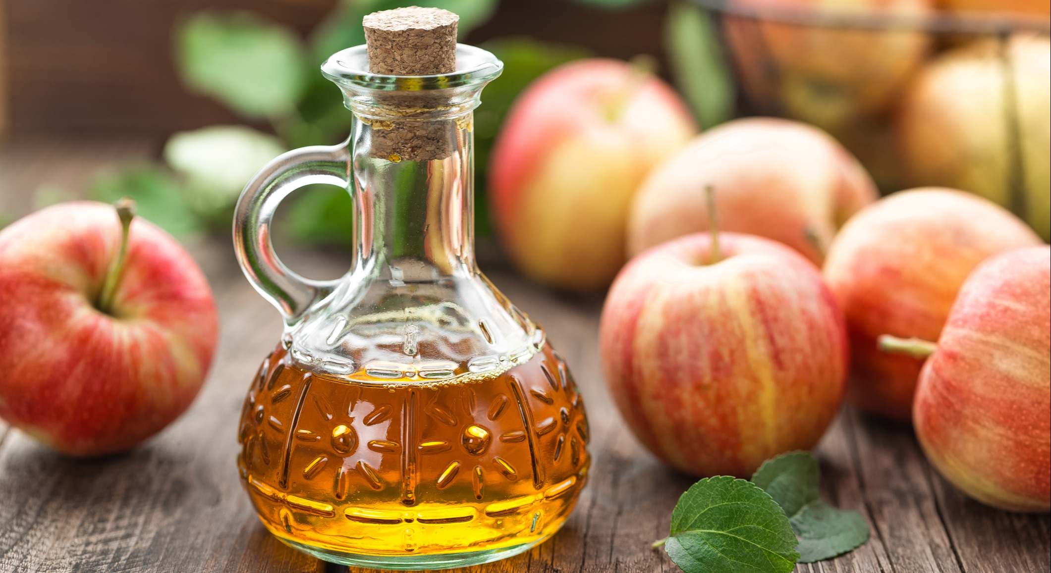 Vinagre de manzana, rodeado de manzanas sobre una mesa de madera