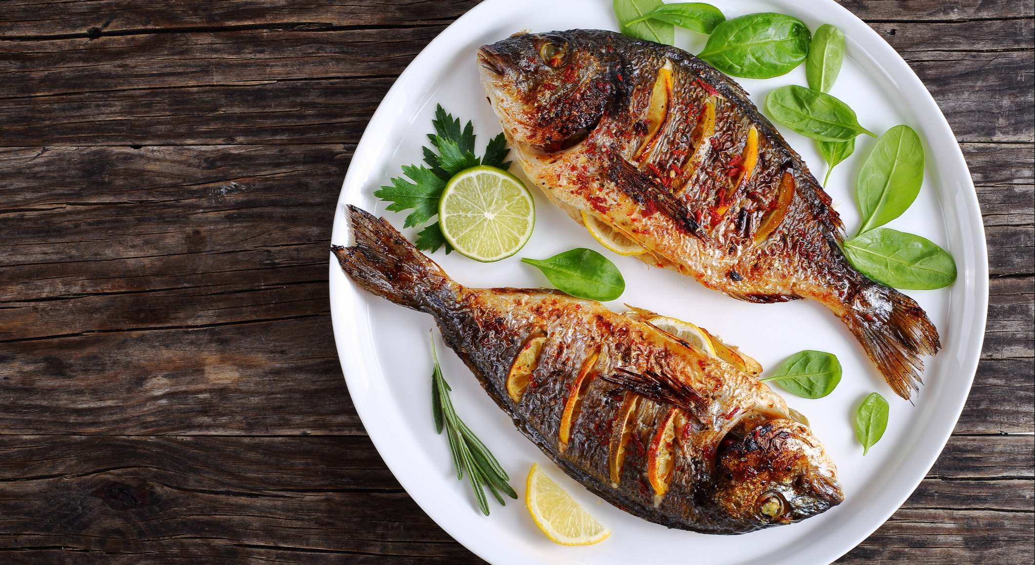 Besugo asado pescado con rodajas de limón en un plato sobre una mesa de madera