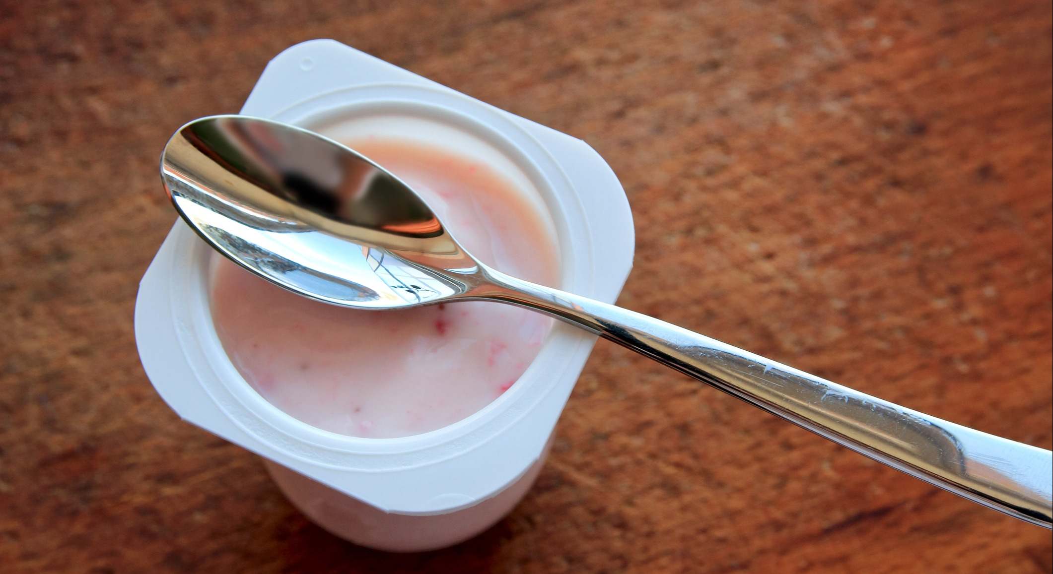 Yogurt de fresa con una cuchara sobre él con un fondo de madera.