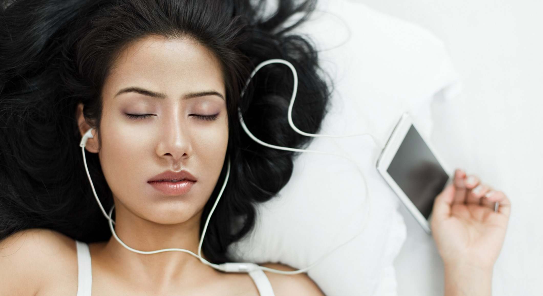 Joven mujer durmiendo con teléfono inteligente y auriculares integrados