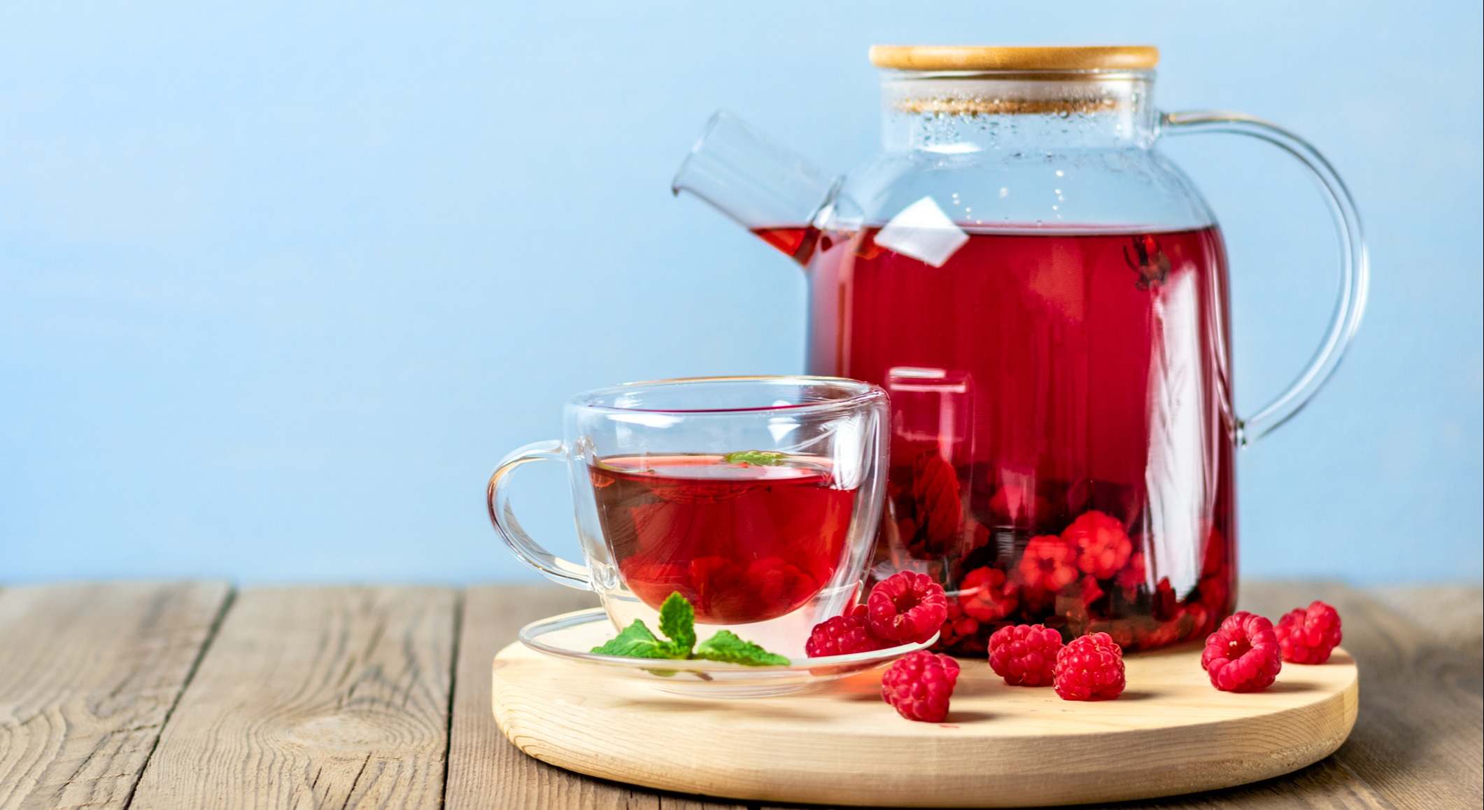 Té de hierbas con bayas, frambuesas, hojas de menta y flores de hibisco en tetera de cristal y taza sobre mesa de madera