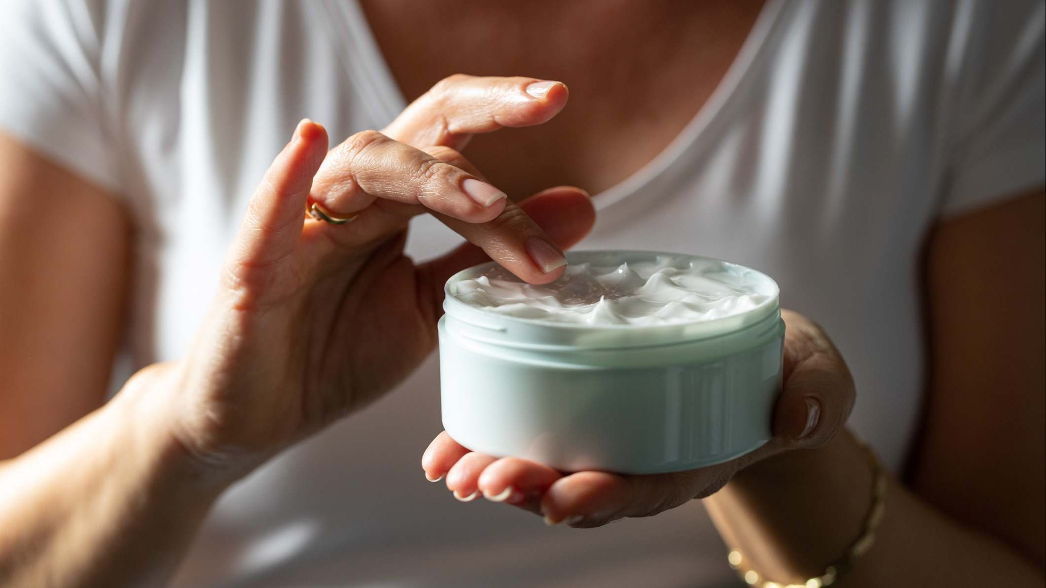 Mujer recoge crema facial con el dedo de un frasco