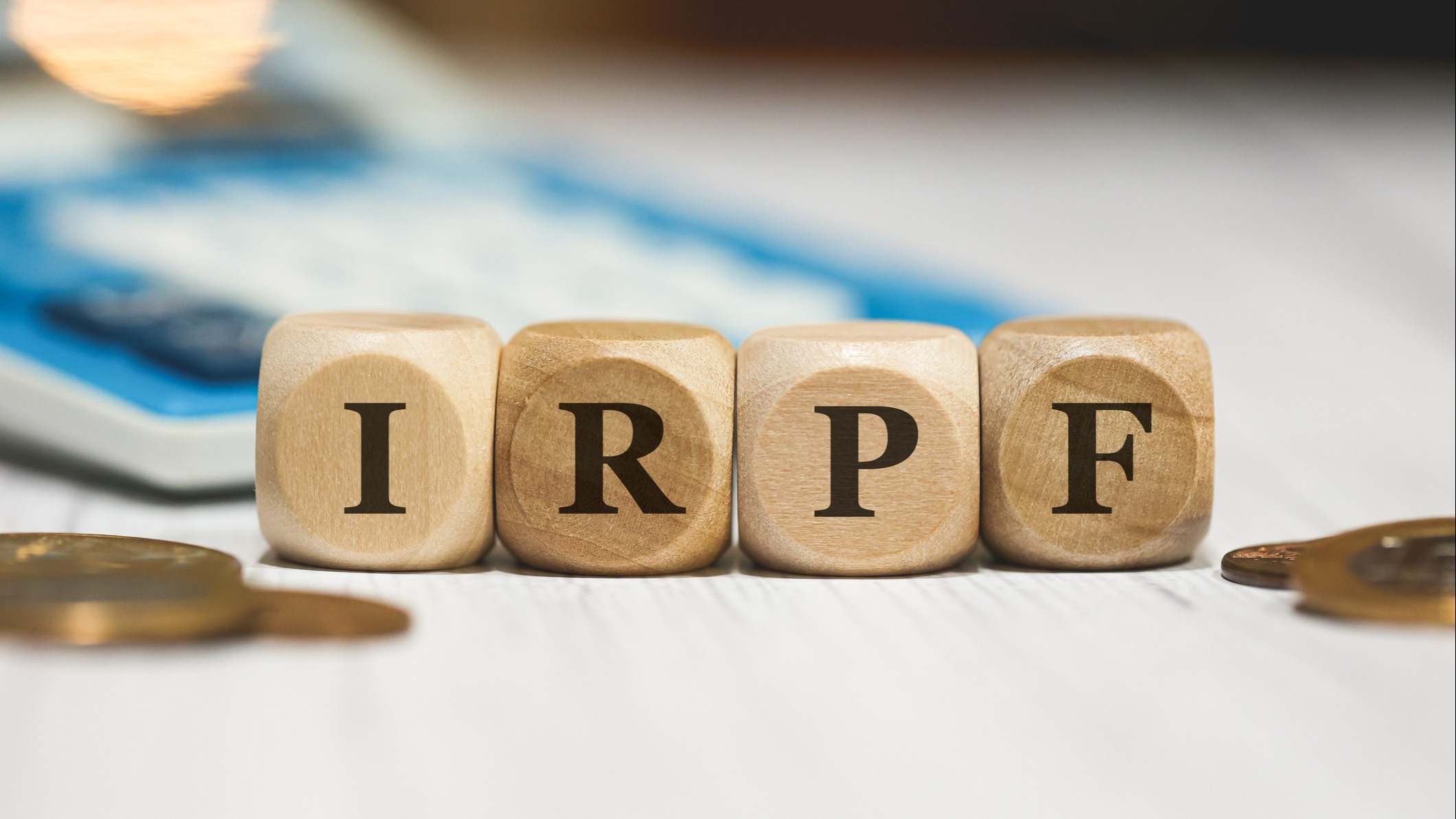 El acrónimo IRPF escrito en dados de madera con monedas y una calculadora de fondo