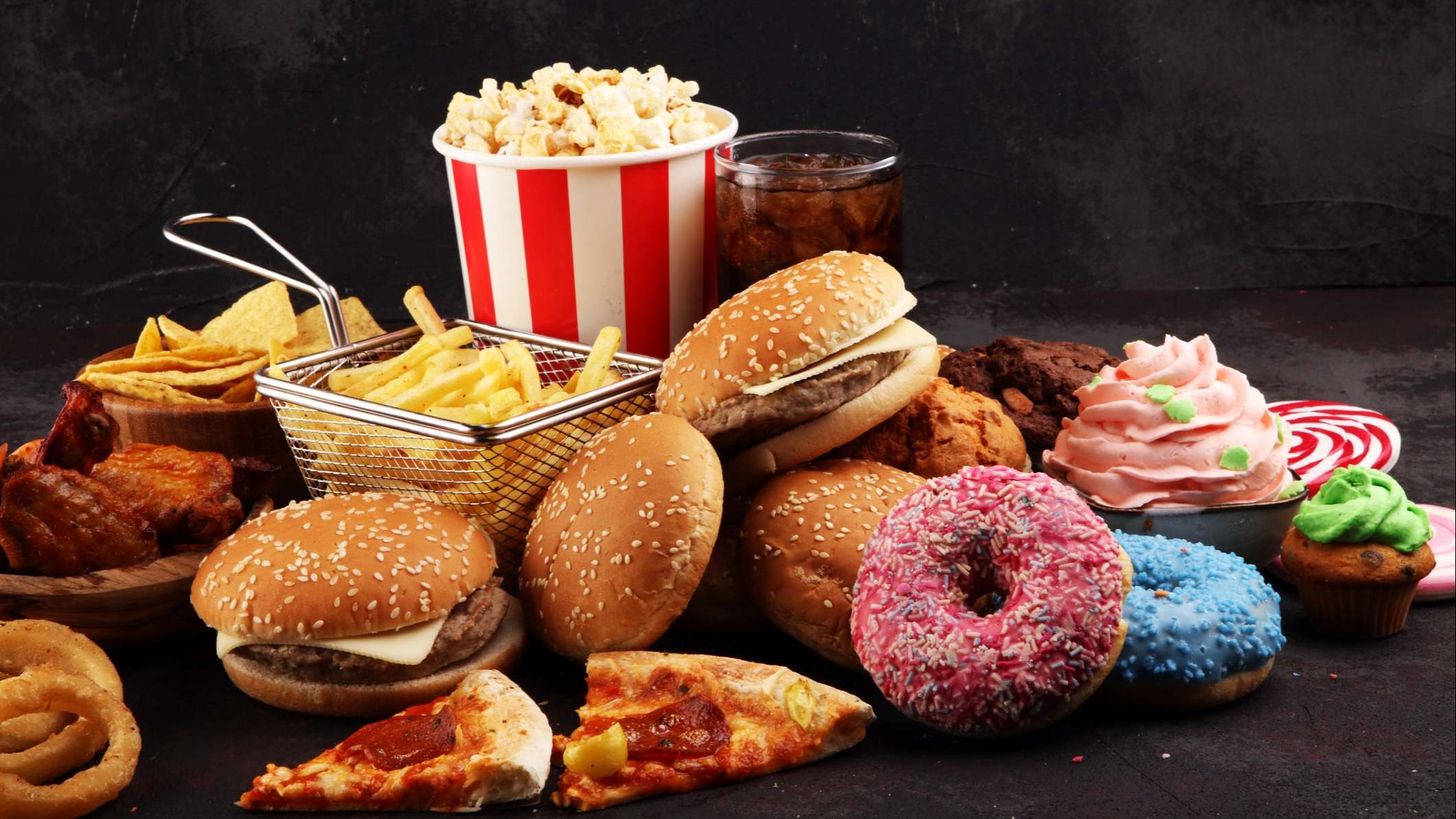 Alimentos ultraprocesados como hamburguesas, pizzas, patatas fritas o dulces sobre un fondo negro