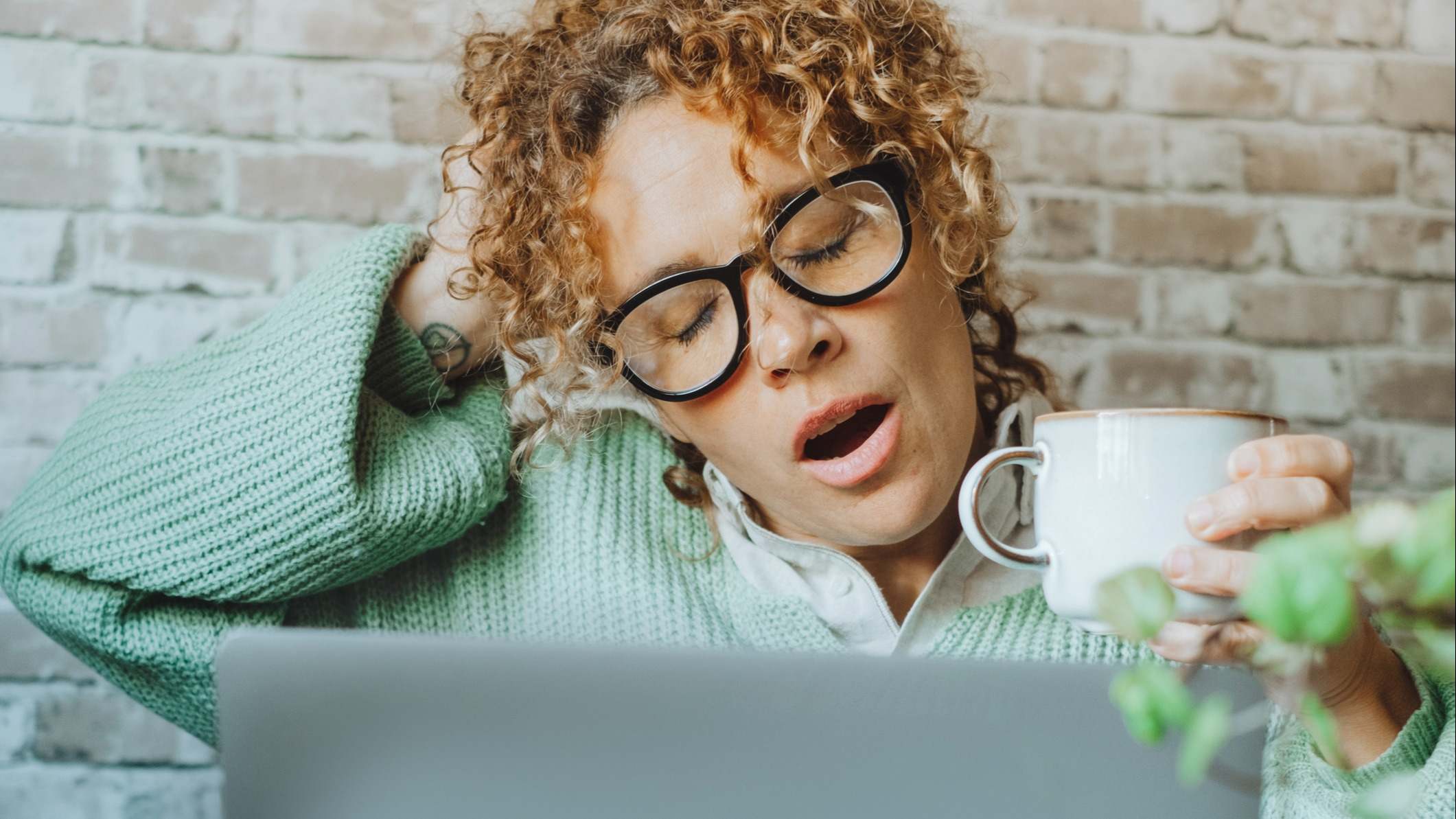 Mujer cansada trabajando delante de su portátil tomando café en una taza