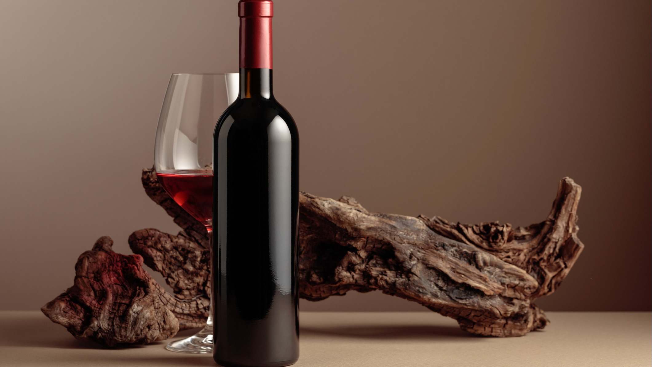 Botella y copa de vino tinto con viejo enganche desgastado sobre un fondo beige.