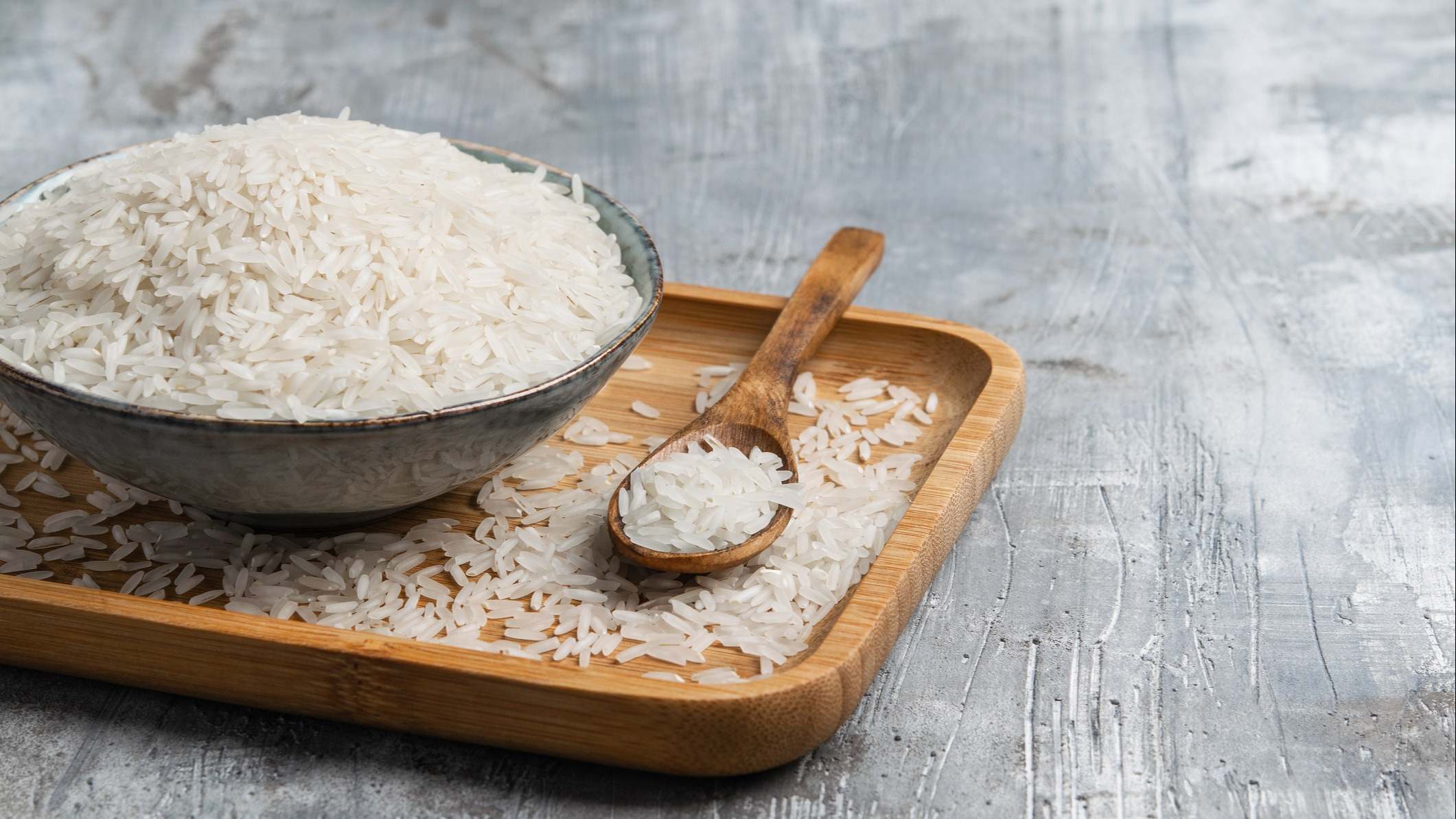 Arroz blanco crudo en tazón de cerámica con cuchara de madera