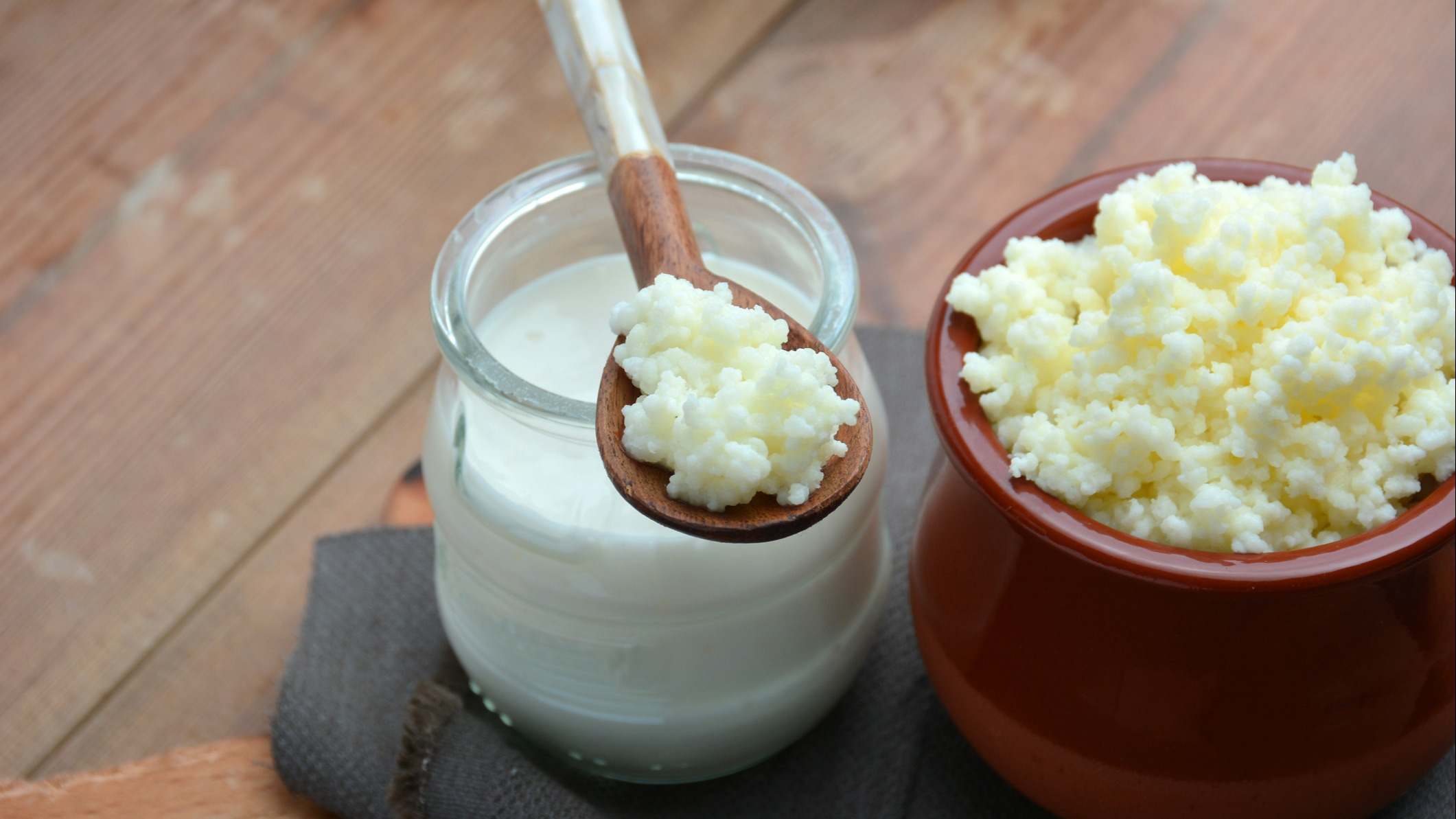 Cucharada de kéfir al lado de un envase lleno de kéfir y otro lleno de leche