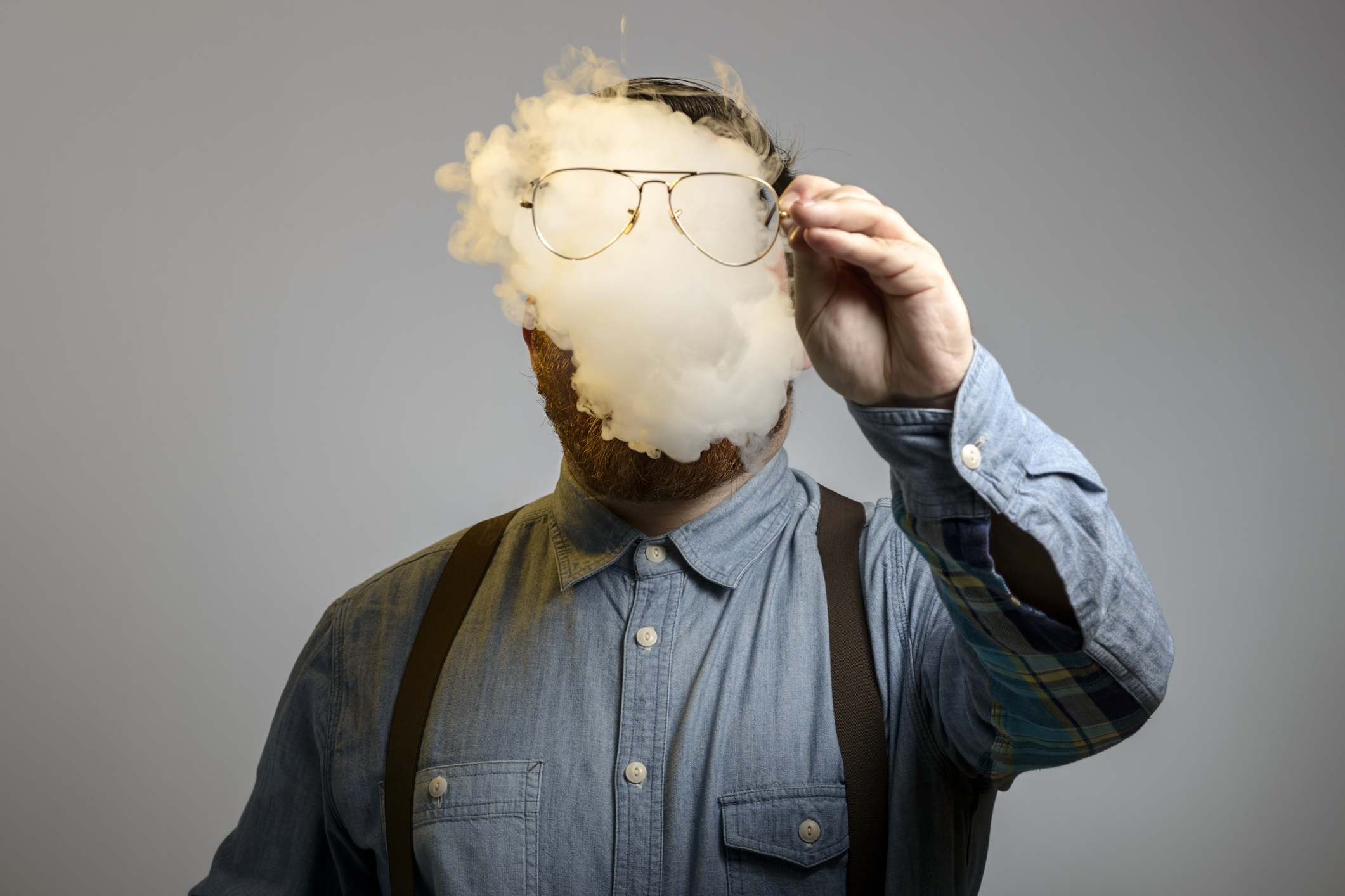 Persona con la cara tapada por el humo sujetando una gafas delante de él