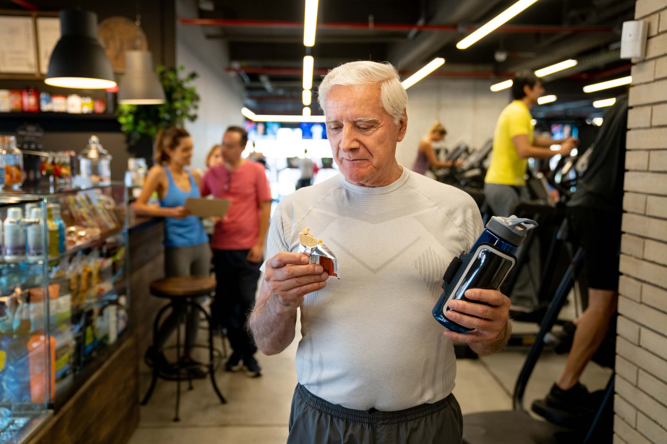 Hombre mayor comiendo una barrita proteica en el gimnasio