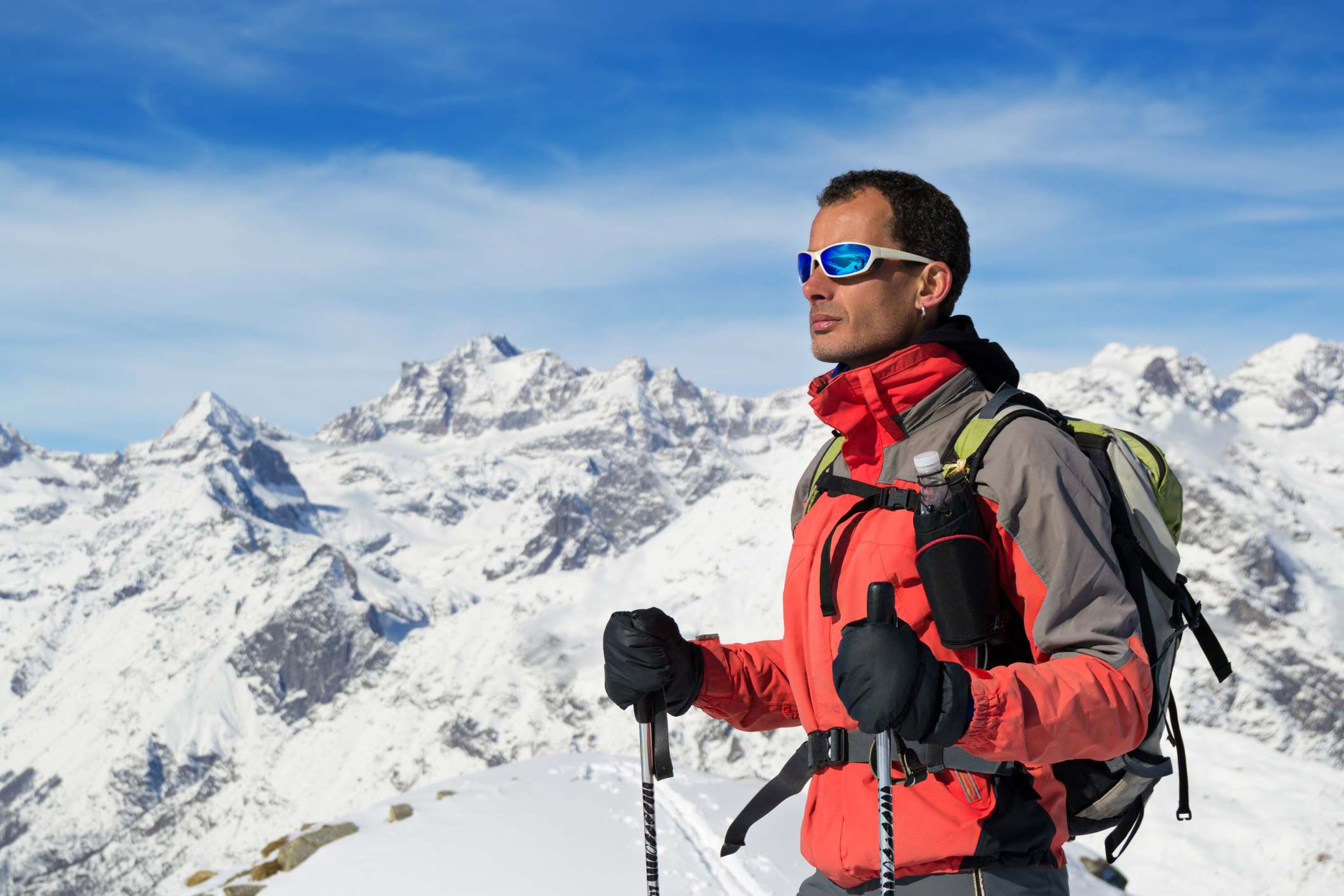 Hombre en ropa de invierno, gafas de sol y palos de esquí en la montaña