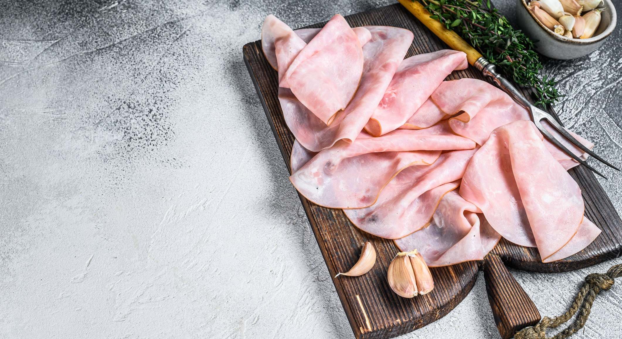 Jamón Fino en rodajas en tabla de cortar de madera con hierbas