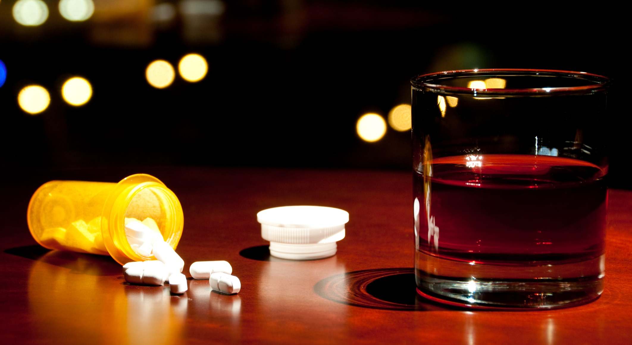 Vaso con alcohol y una bote de pastillas sobre una mesa