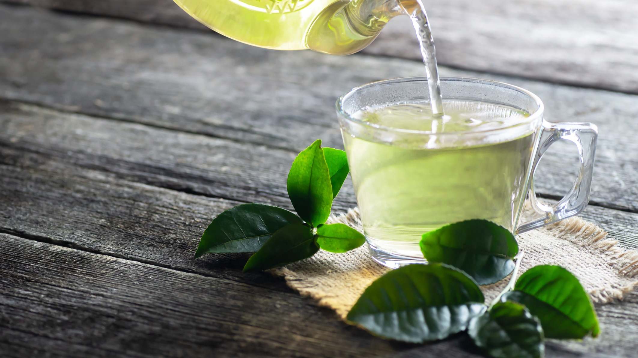 Taza de cristal de té verde con hojas de té fresco sobre mesa de madera