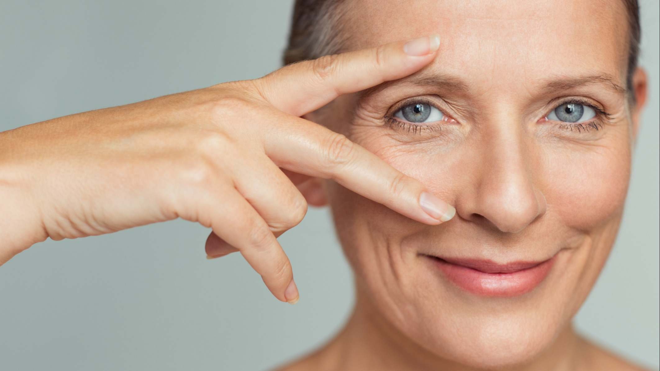Mujer de mediana edad con su rostro en primer plano señalándose los ojos